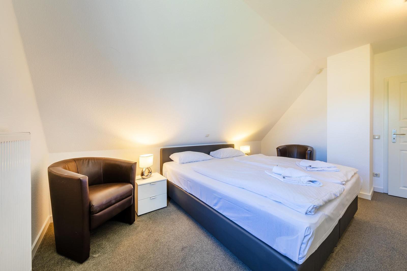 Schlafzimmer mit Doppelbett, zwei Nachttischen und braunen Sesseln.