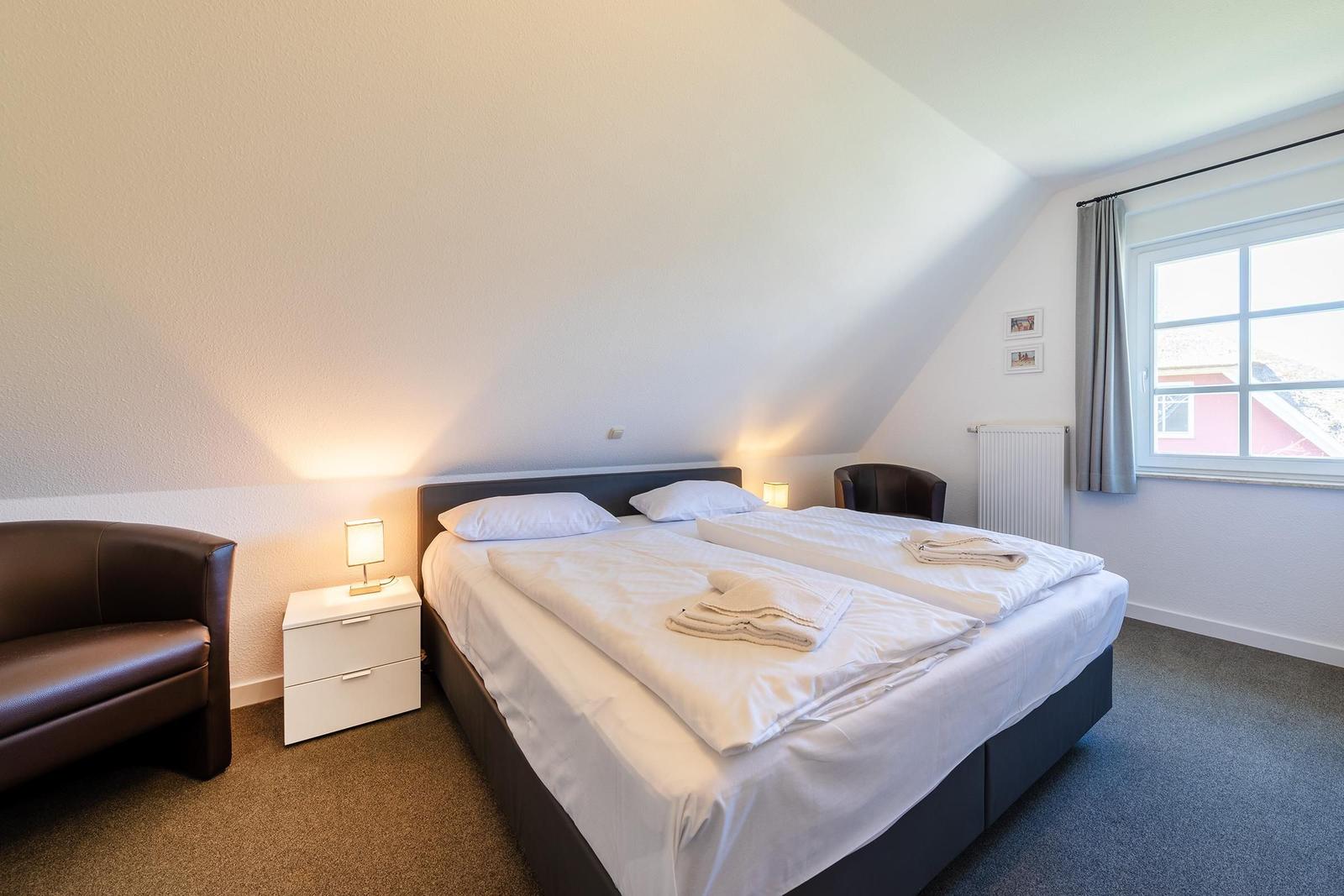 Doppelbettzimmer mit Schreibtisch, Lampe und Fenster. Dachgeschoss mit schrägen Wänden.