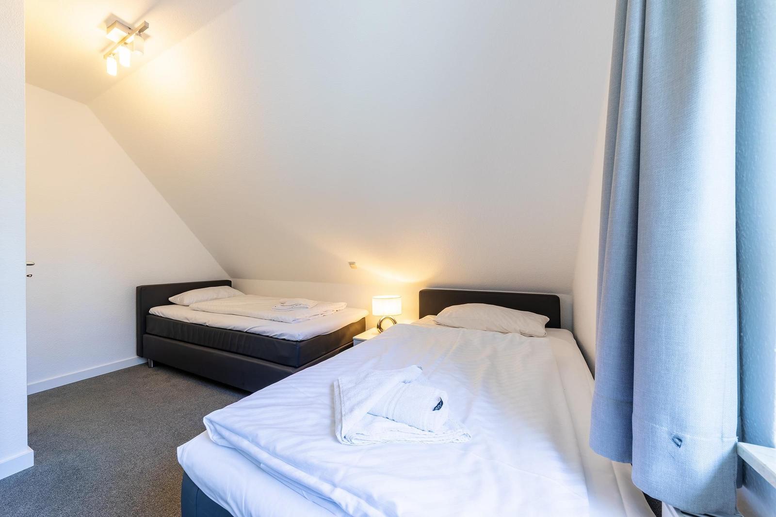Zwei Betten in einem Dachzimmer mit Steigungsdecke und grauem Teppichboden.