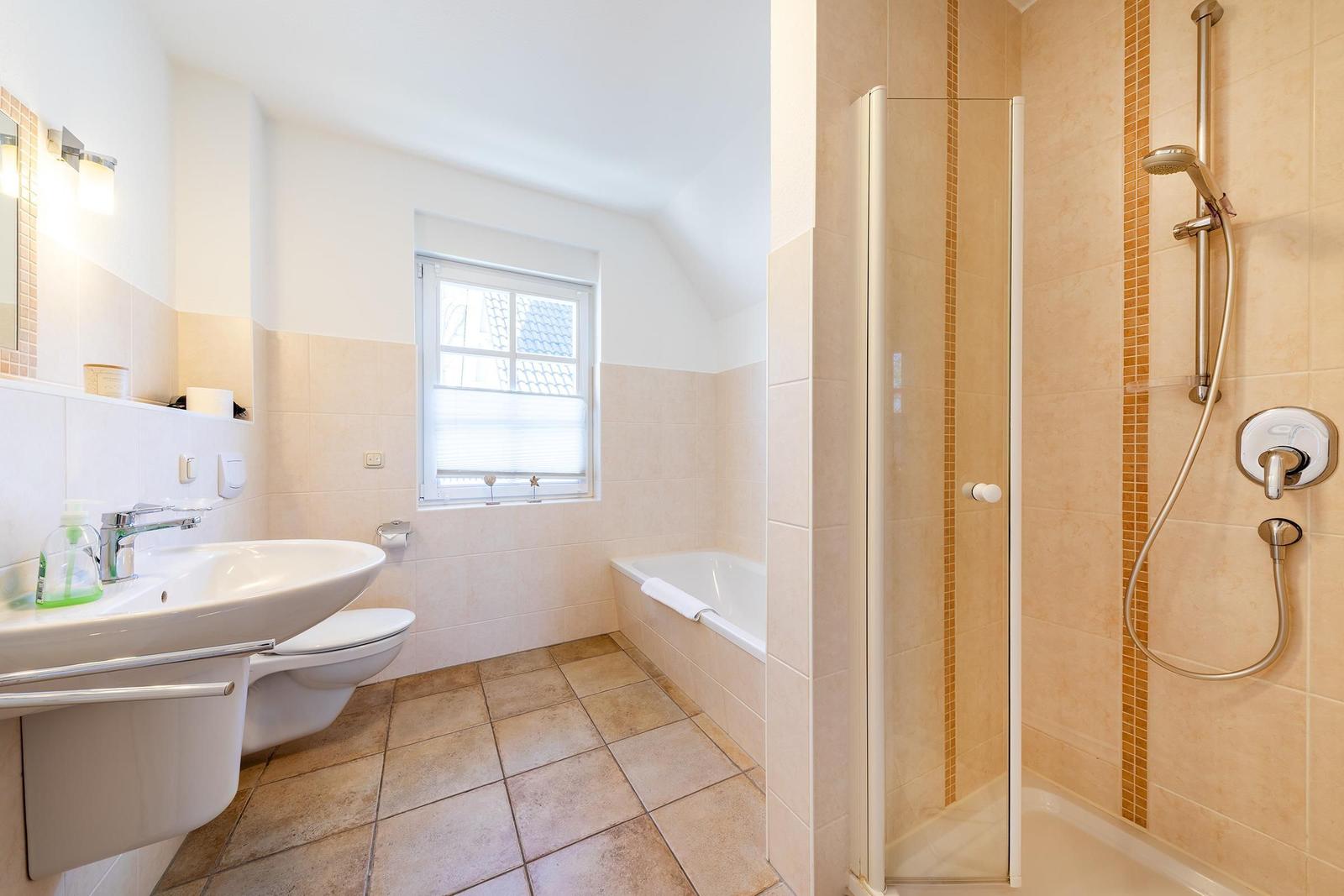 Badezimmer mit Dusche, Badewanne und Waschbecken. Fenster mit Jalousie.