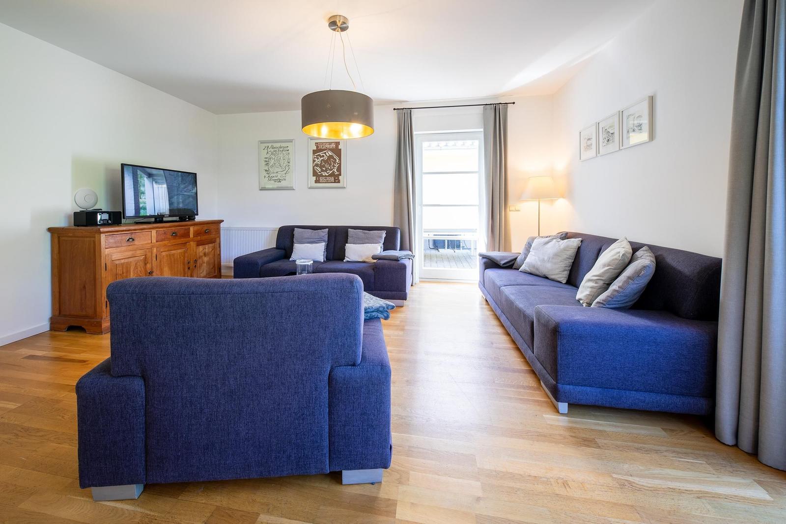 Wohnzimmer mit blauen Sofas, Holzboden und Fernseher auf Holzschrank.