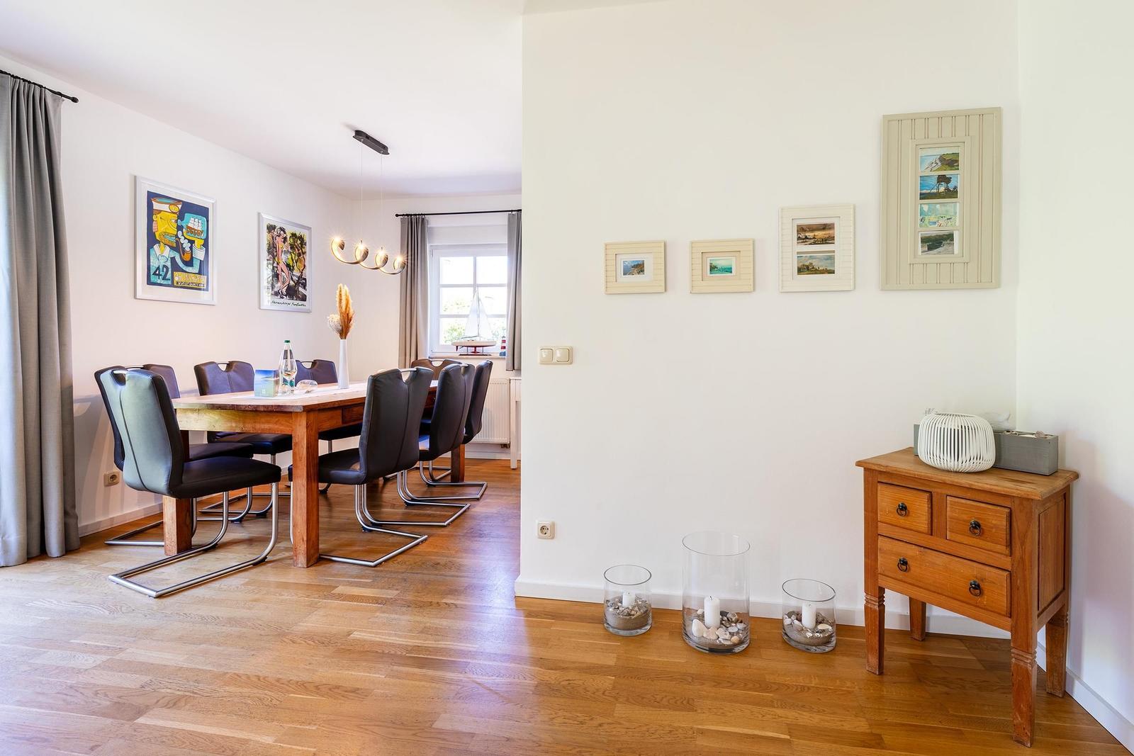 Esszimmer mit Holztisch, Stühlen und Wandbildern. Nebenraum mit Schrank und Dekorationsgegenständen.