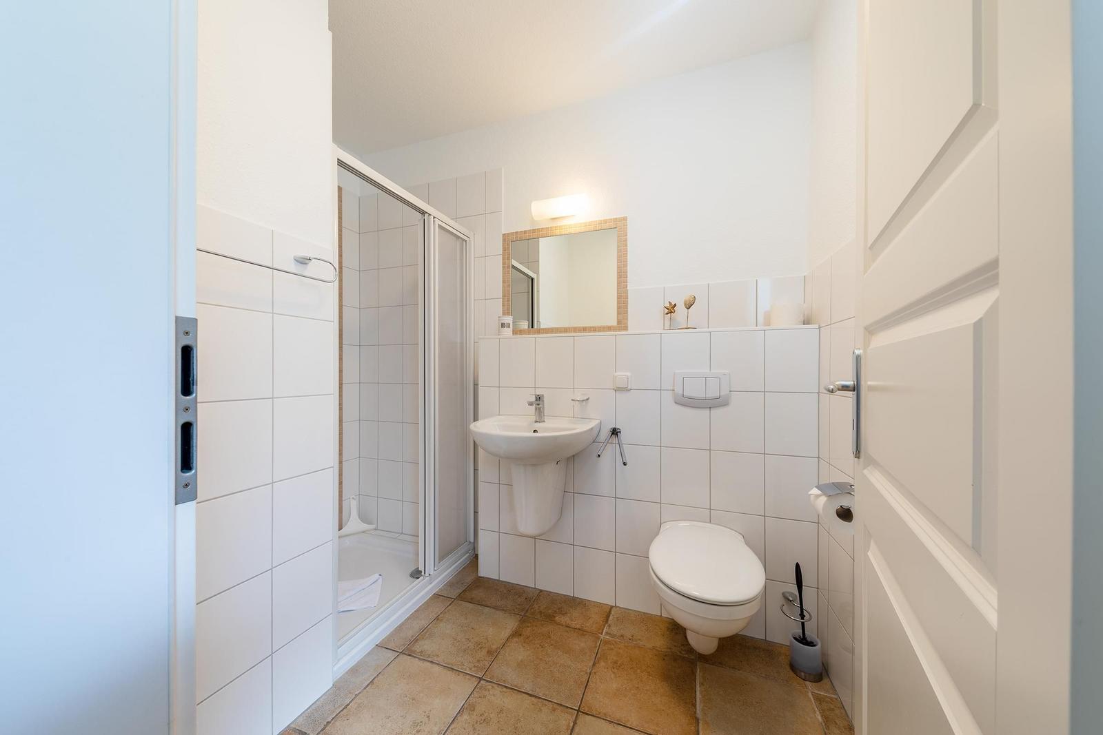 Badezimmer mit Dusche, Waschbecken und Toilette. Fliesenboden und Wandfliesen.