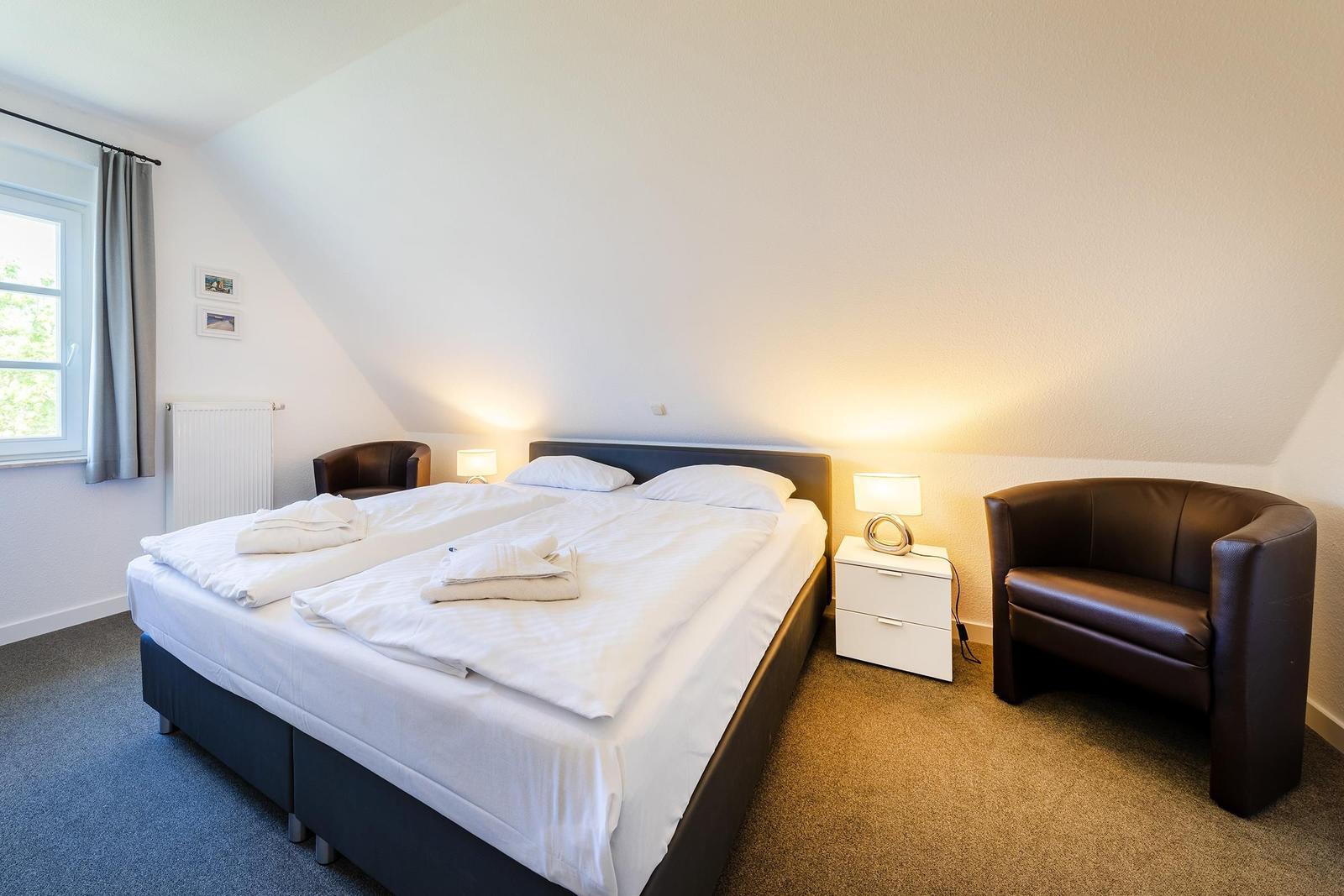 Schlafzimmer mit Doppelbett, zwei Sesseln und Nachttisch unter Dachschrägen.