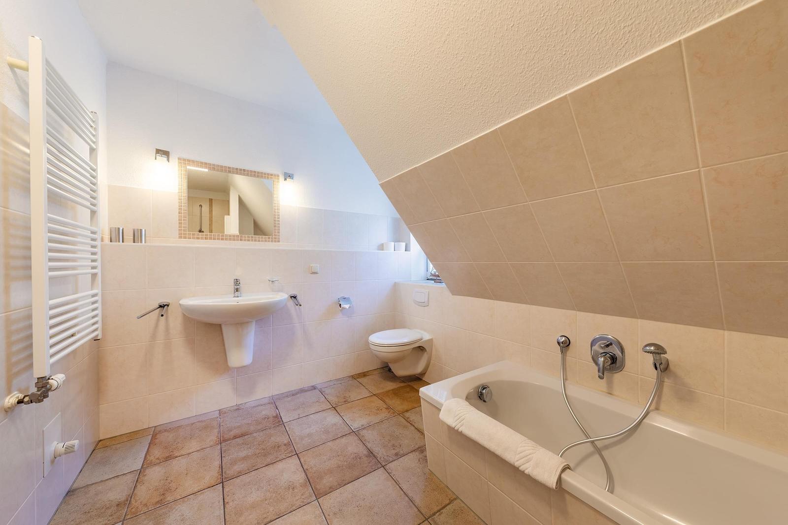 Badezimmer mit Badewanne, Toilette und Waschbecken unter schräger Decke.