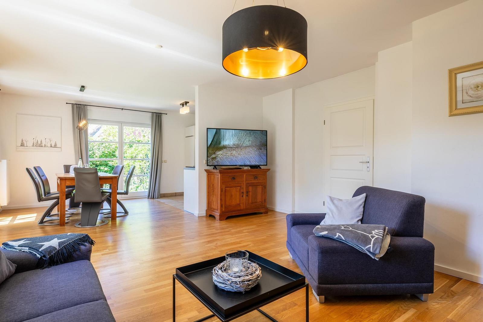Wohn- und Essbereich mit Holzboden, Sofa, Fernseher und Tisch mit Stühlen.