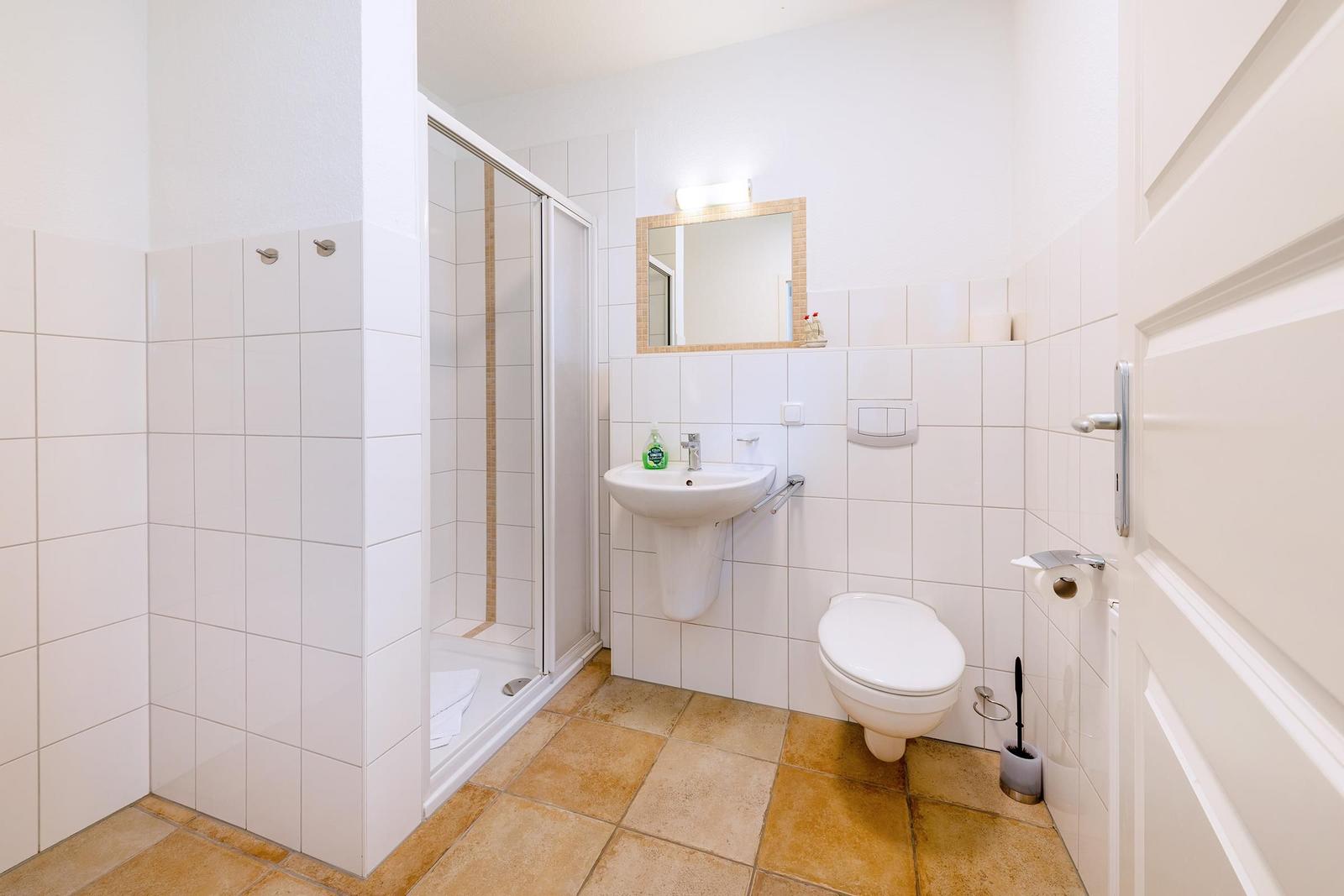 Badezimmer mit Dusche, Waschbecken und Toilette. Fliesenwand und Bodenfliesen.