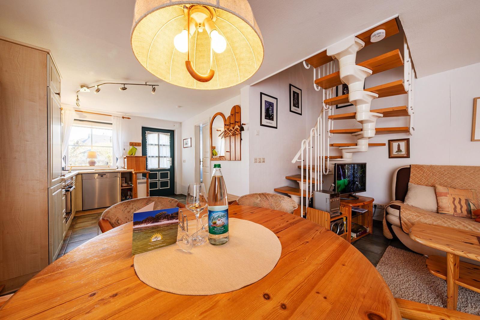 Essbereich mit Holztisch, Spindelstiege und Sofa im Wohnbereich.