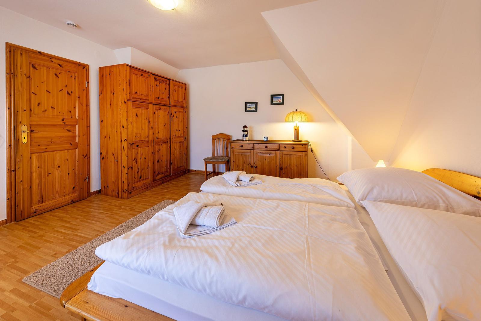 Schlafzimmer mit Doppelbett, Holzmöbel und schräger Decke.