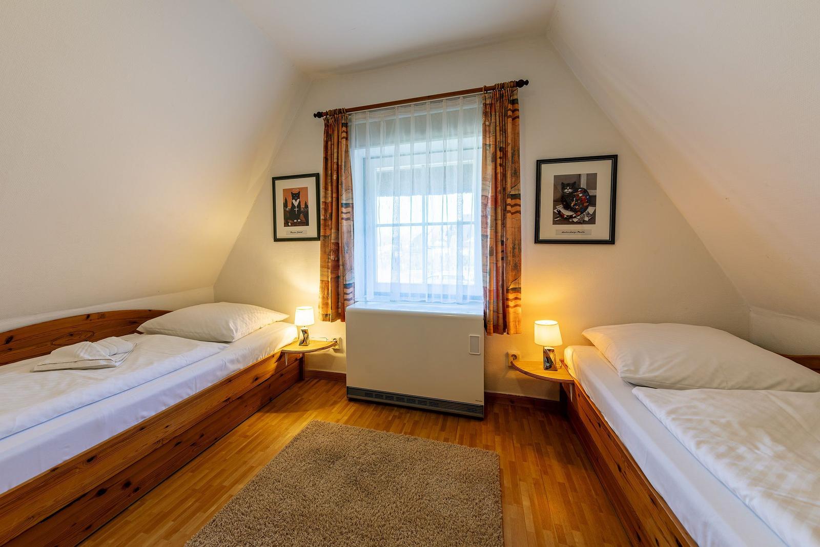 Zimmer mit zwei Betten, Fenster, Heizung und Teppichboden.
