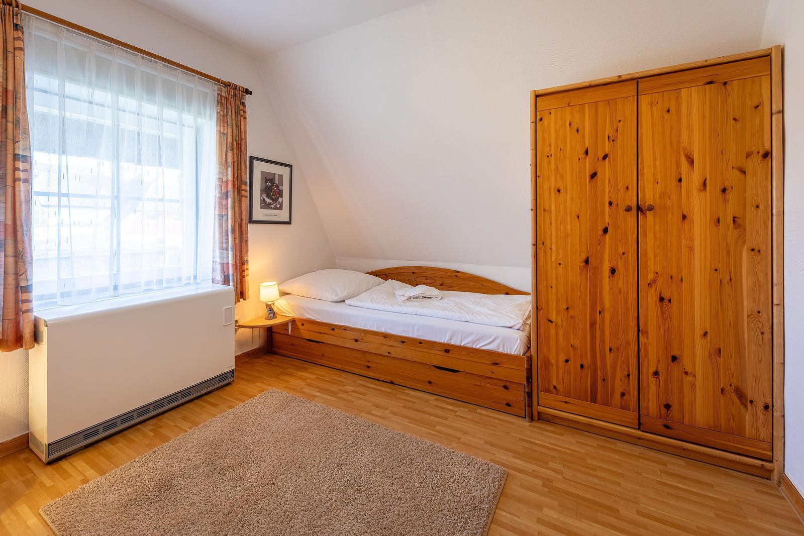 Schlafzimmer mit Holzbett, Kleiderschrank und Fenster mit Vorhängen.