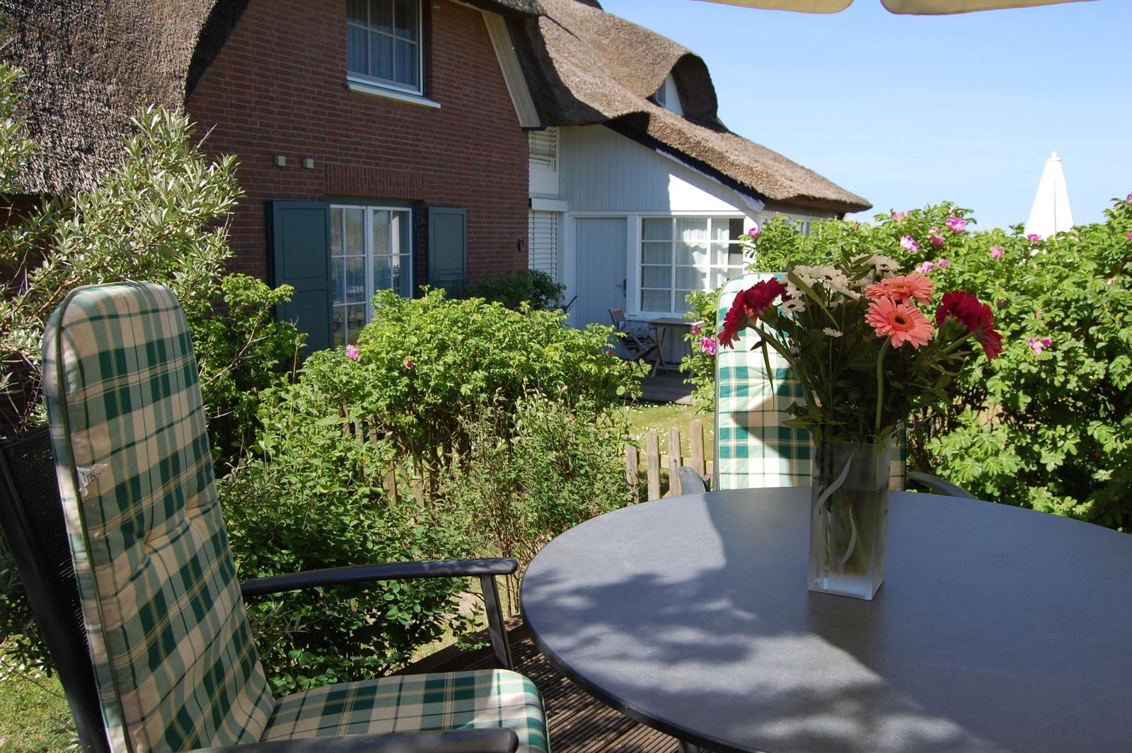 Terrasse mit Tisch, Stühlen und Blumen vor einem Haus mit Strohdach.