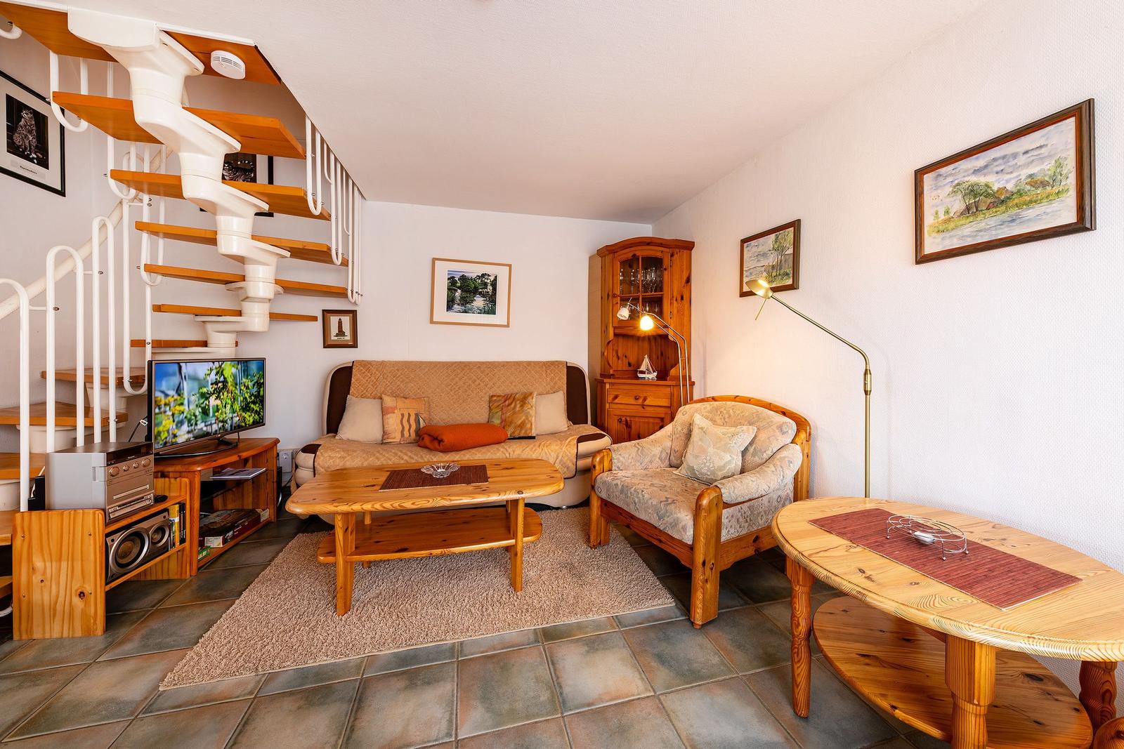 Wohnzimmer mit Holzmöbeln, Fernseher und Treppe zur oberen Etage.