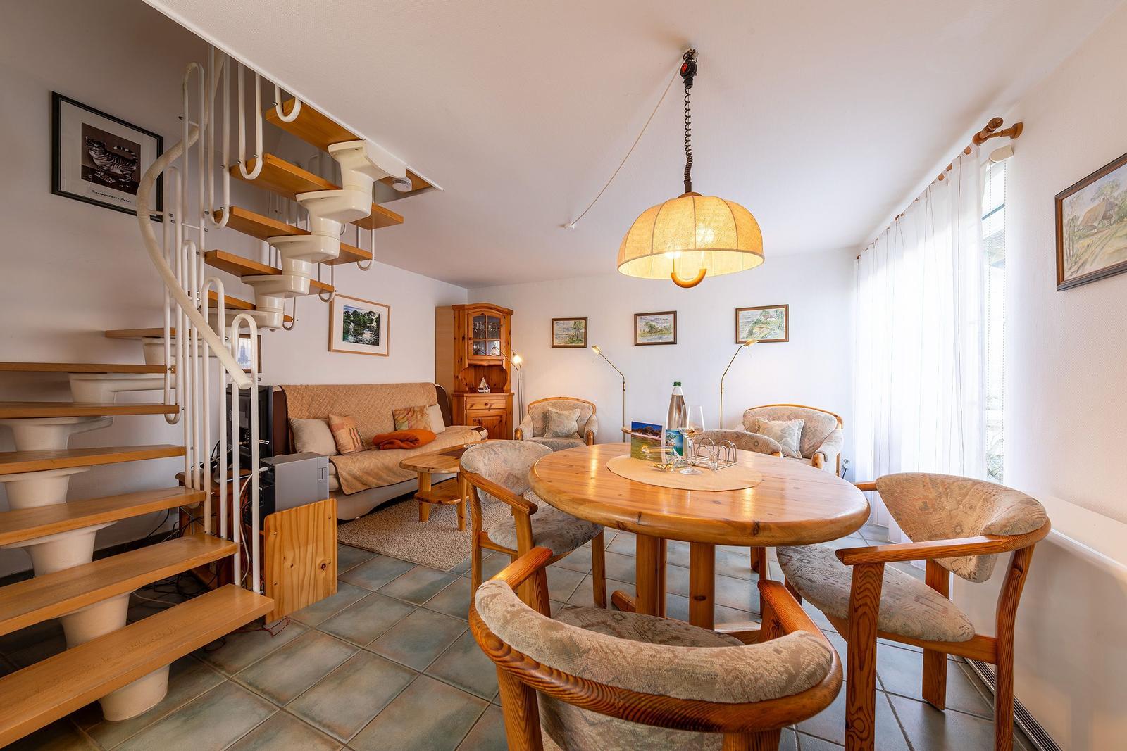 Esszimmer mit Holztisch, Stühlen und Wohnbereich mit Sofa und Treppe.