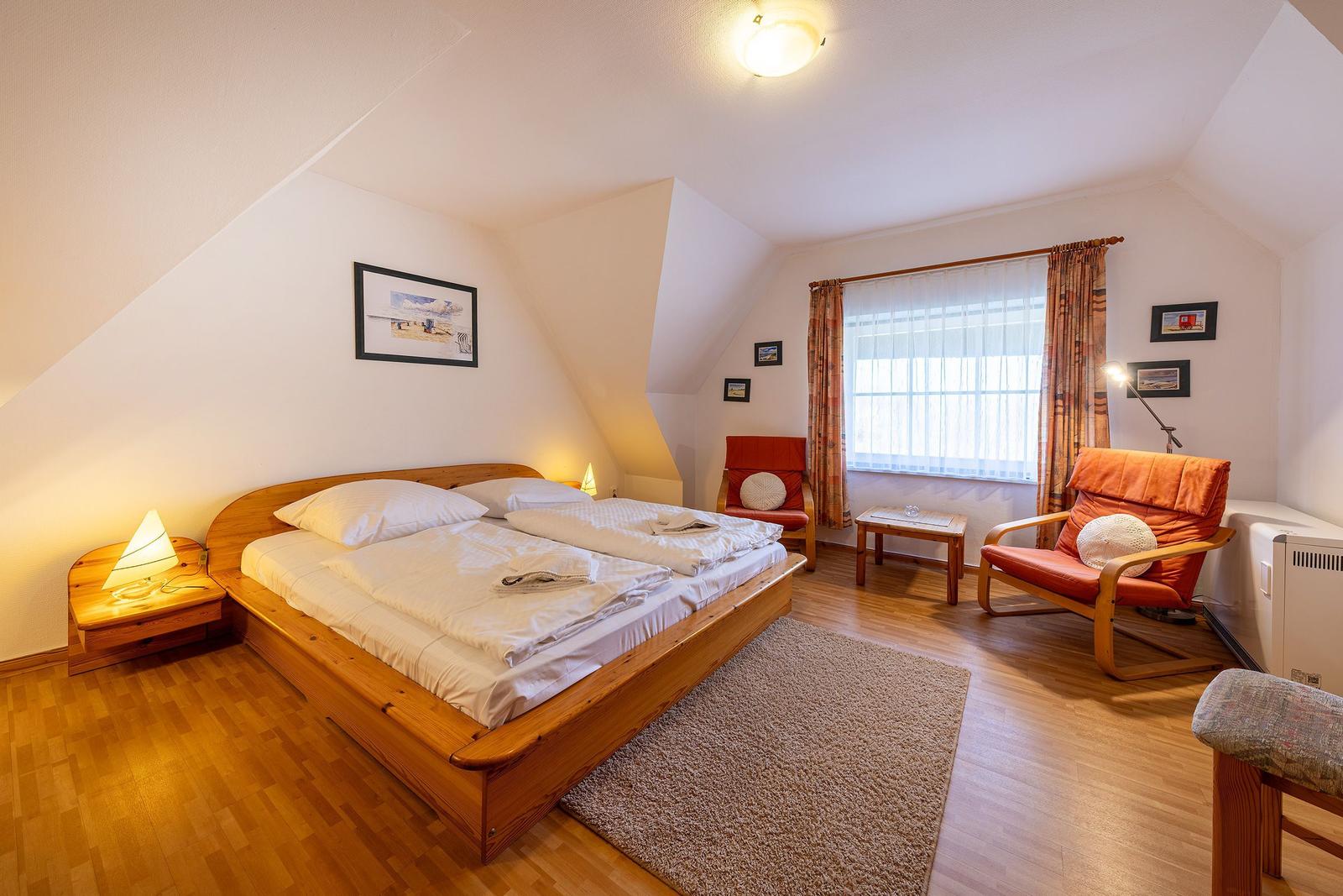 Schlafzimmer mit Doppelbett, zwei Sesseln und Holzboden unter schrägen Wänden.