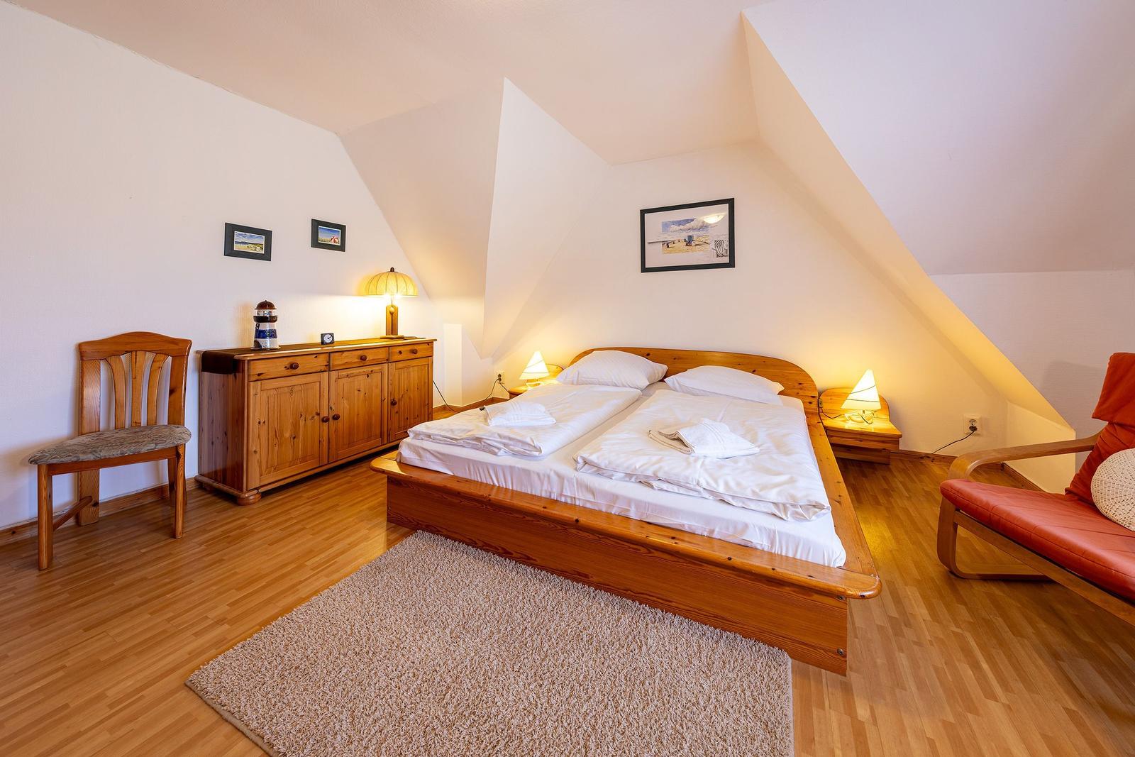 Doppelbettzimmer mit Holzboden, Schrank, Stuhl und Sessel unter Dachschrägen.