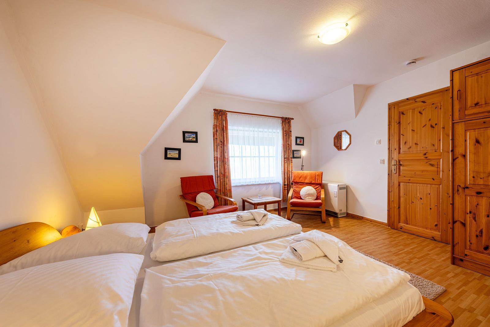 Schlafzimmer mit Doppelbett, zwei roten Sesseln und Holzmöbeln.