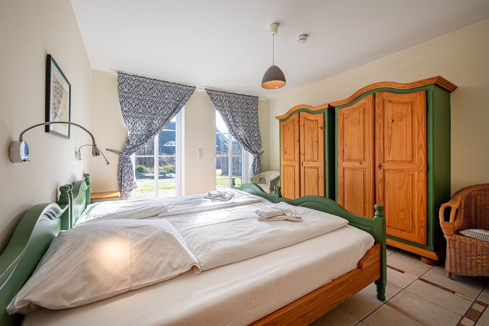 Schlafzimmer mit Doppelbett, Holzschrank und Fenster zur Außenterrasse.
