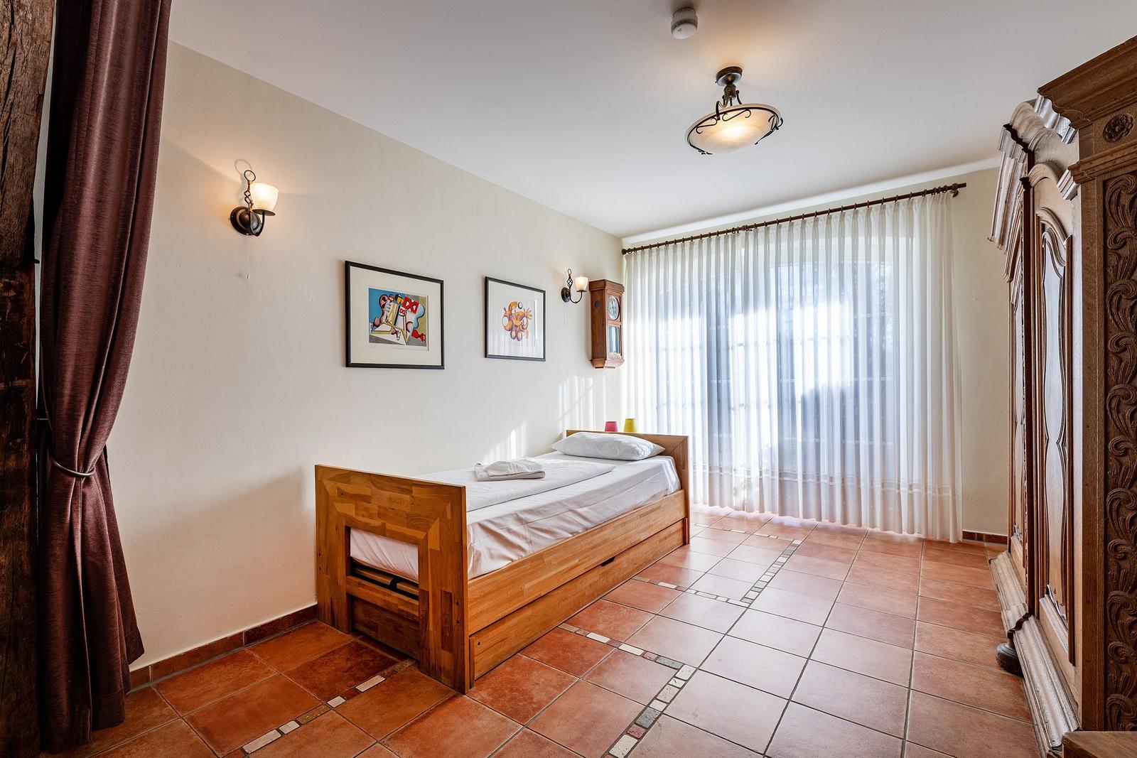 Ein Schlafzimmer mit Holzbett, Wandbildern, Vorhängen und Fliesenboden.