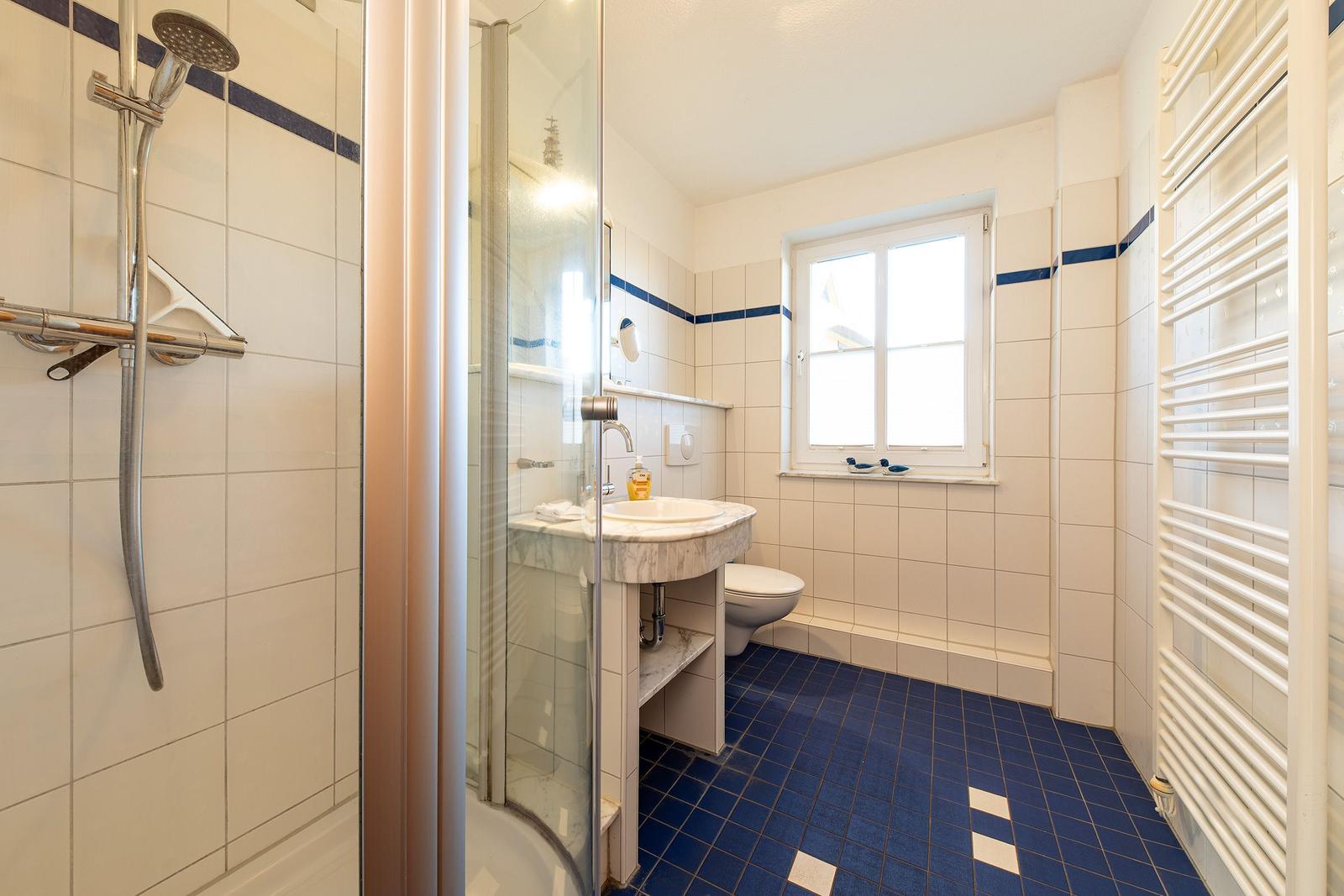Badezimmer mit Dusche, Waschbecken und Toilette. Blaue Fliesen und Fenster.