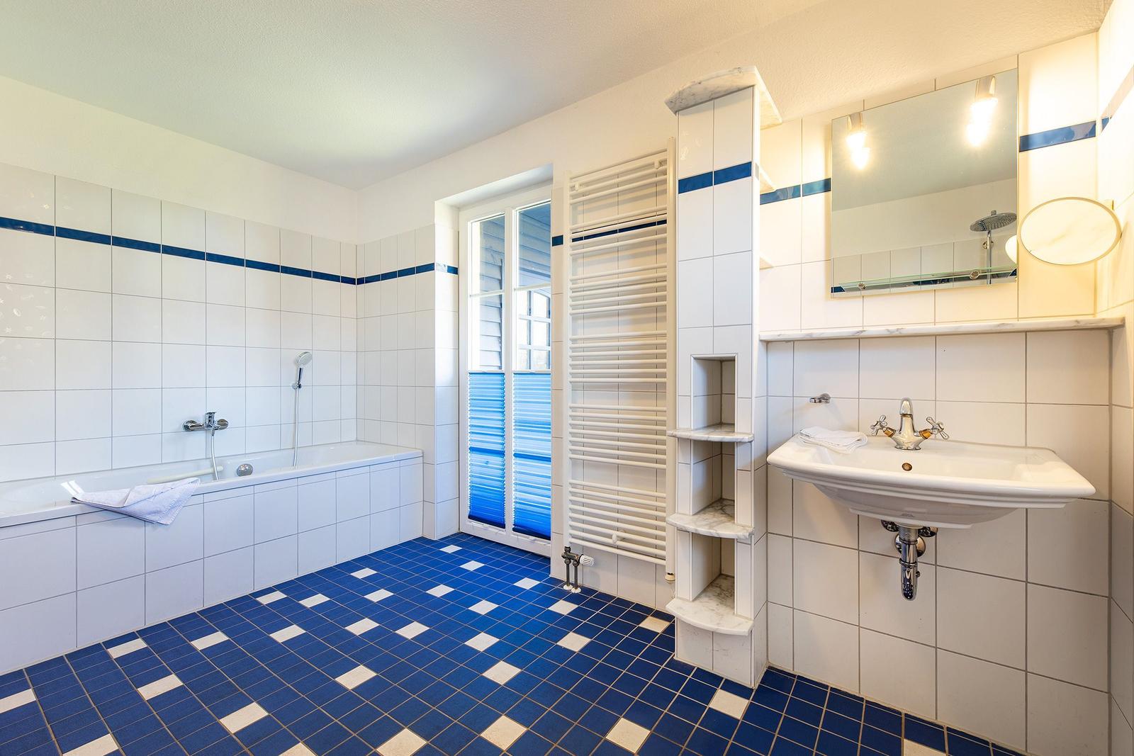 Badezimmer mit Badewanne, Waschbecken und Heizkörper. Bodenfliesen blau-weiß.