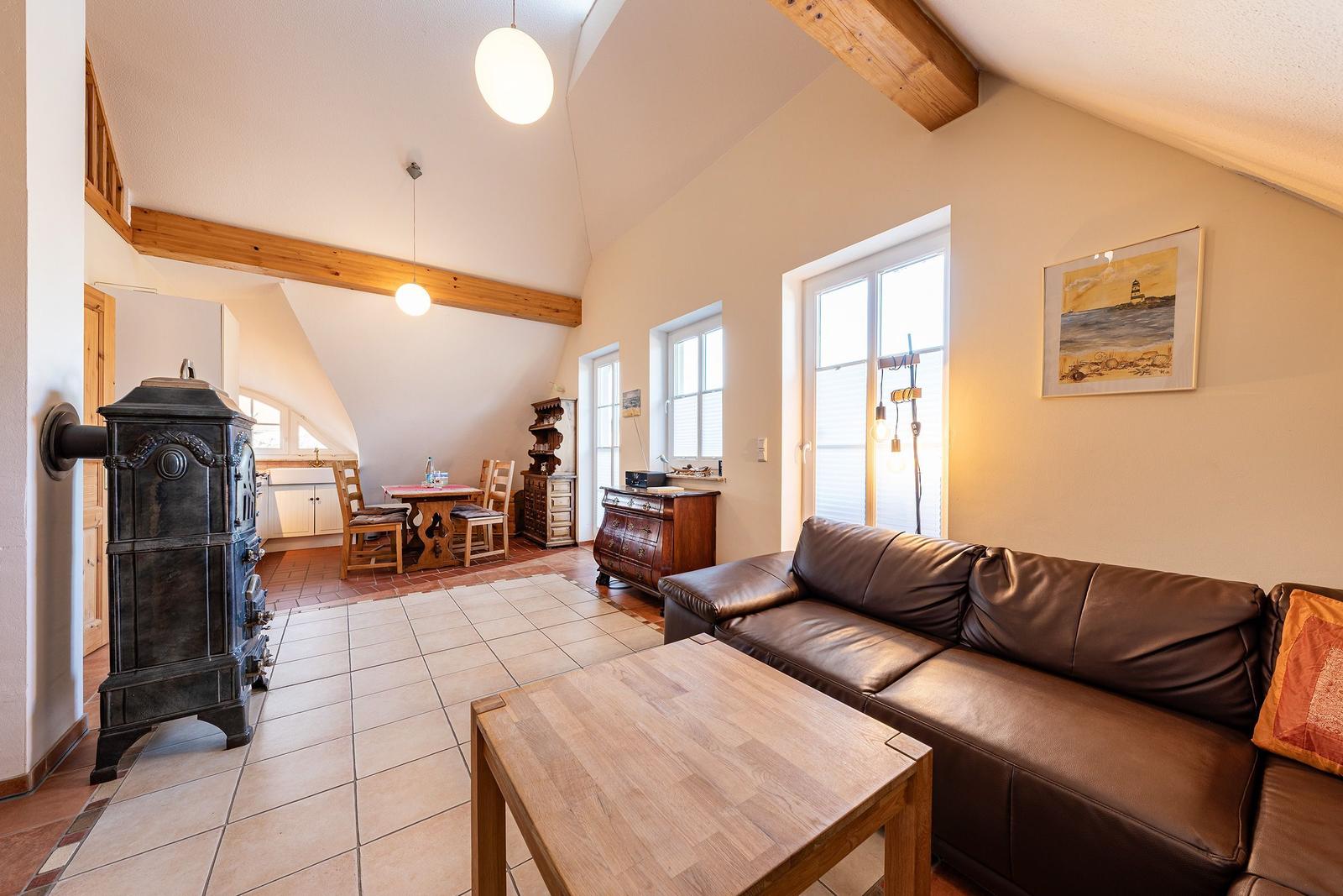 Wohn- und Essbereich mit Holzdecke, Sofa und Kaminofen. Küche im Hintergrund.