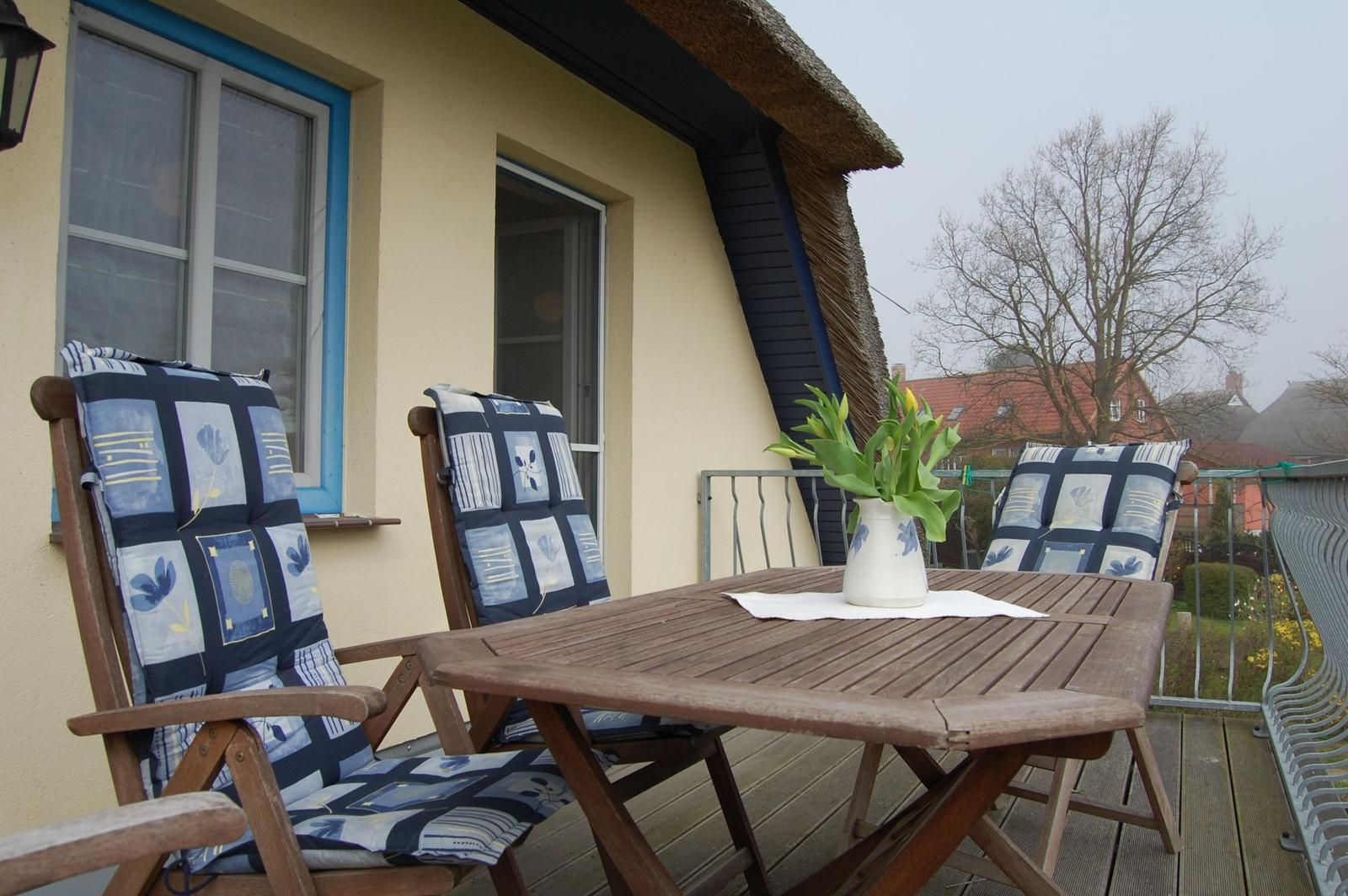 Terrasse mit Holztisch, drei Stühlen und Blumen im Vase.