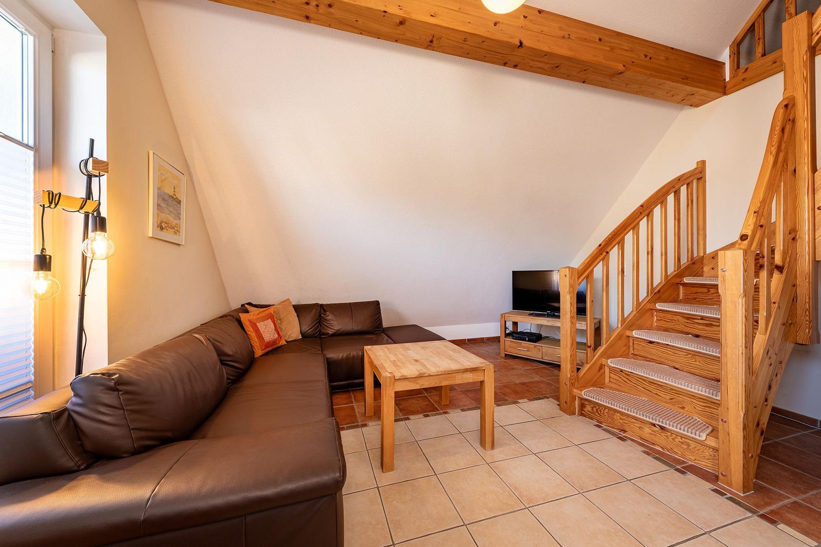 Wohnbereich mit braunem Sofa, Holztisch und Holztreppe
