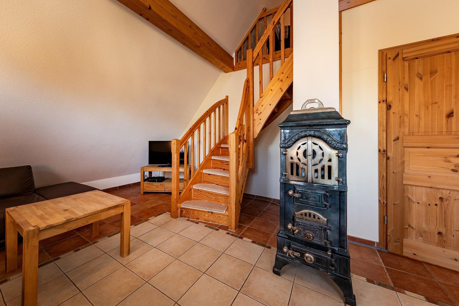 Wohnzimmer mit Holztreppe, Kaminofen und Sofa auf Terrakottboden