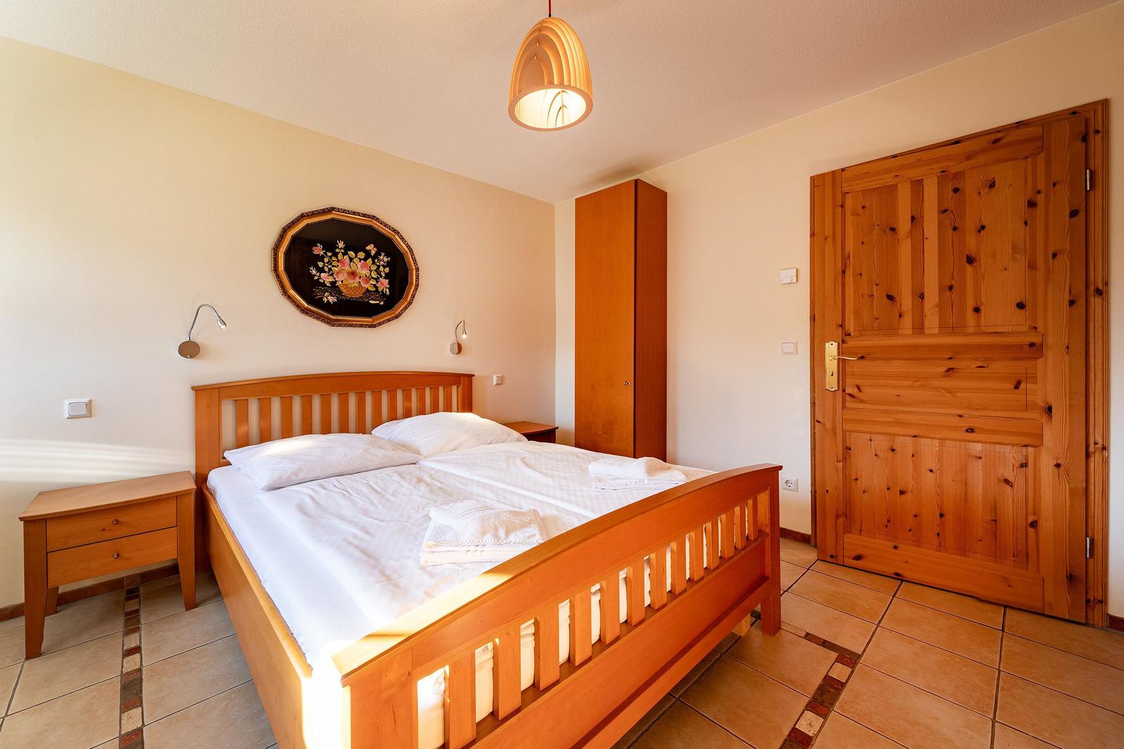 Schlafzimmer mit Holzbett, Nachttisch, Kleiderschrank und Holztür.