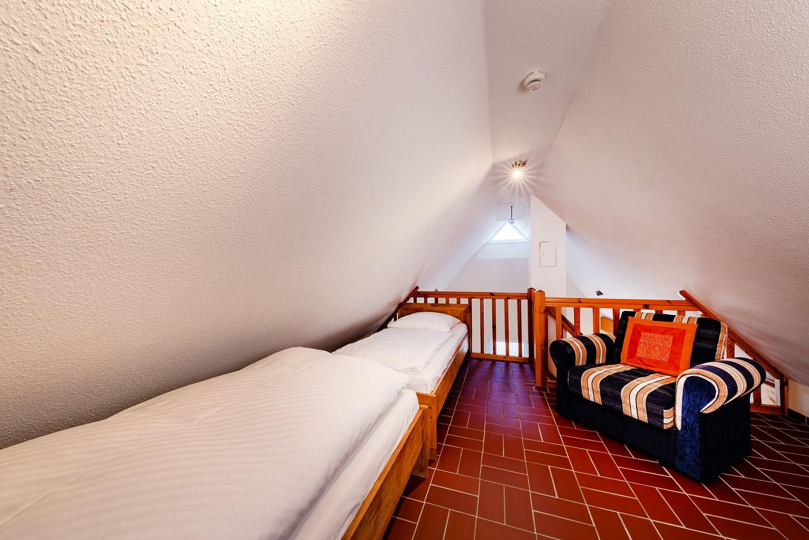 Zimmer mit zwei Betten und Sitzgelegenheit unter Dachschrägen.
