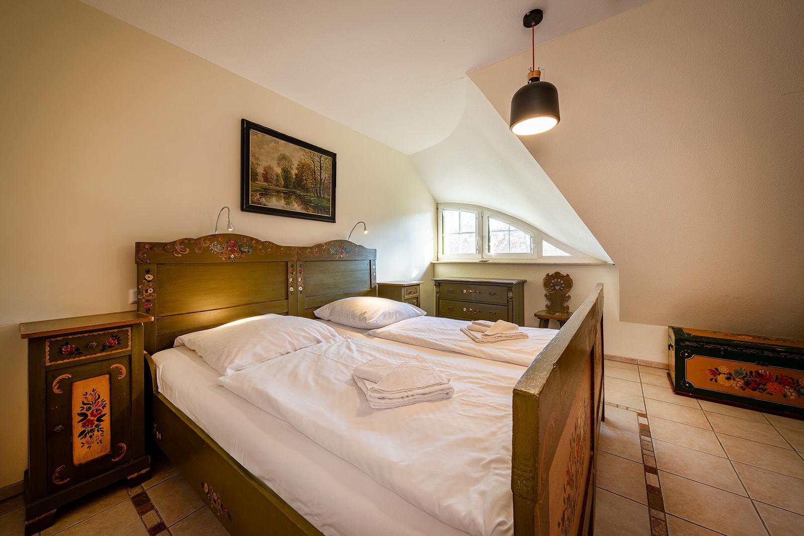 Schlafzimmer mit Bett, Nachttisch und Fenster unter Dachschrägen.
