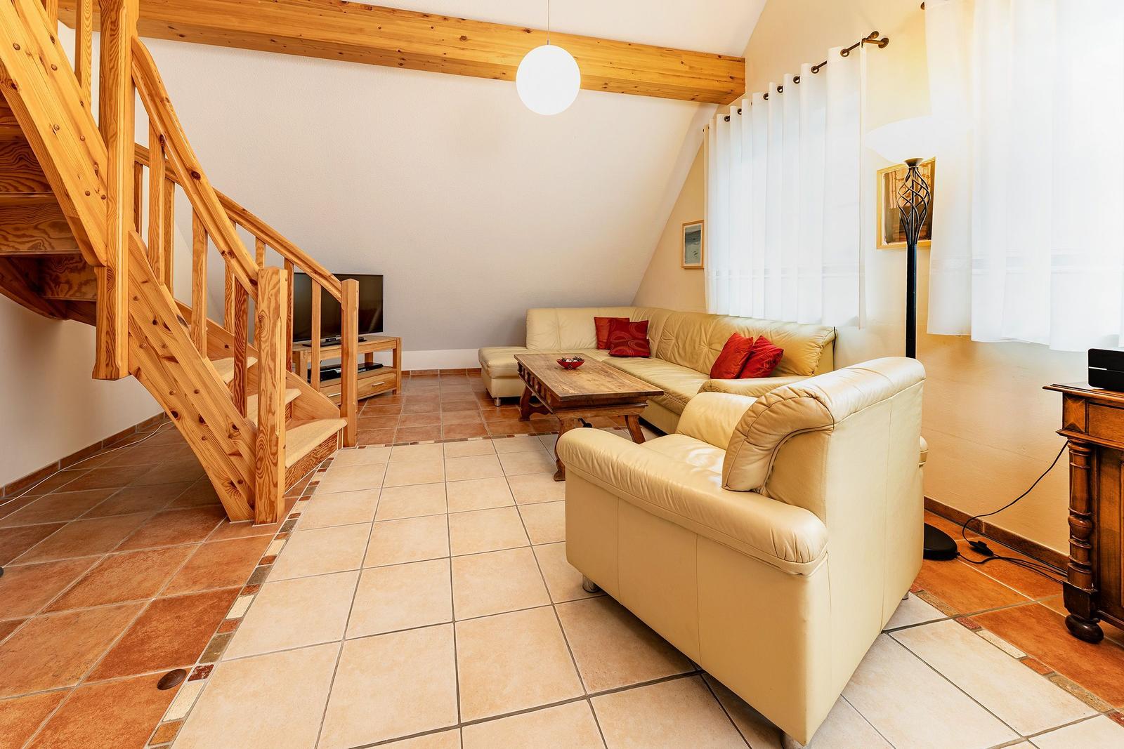 Wohnzimmer mit Holztreppe, Sofa, Couchtisch und TV. Terrakottafußboden und Holzbalken.