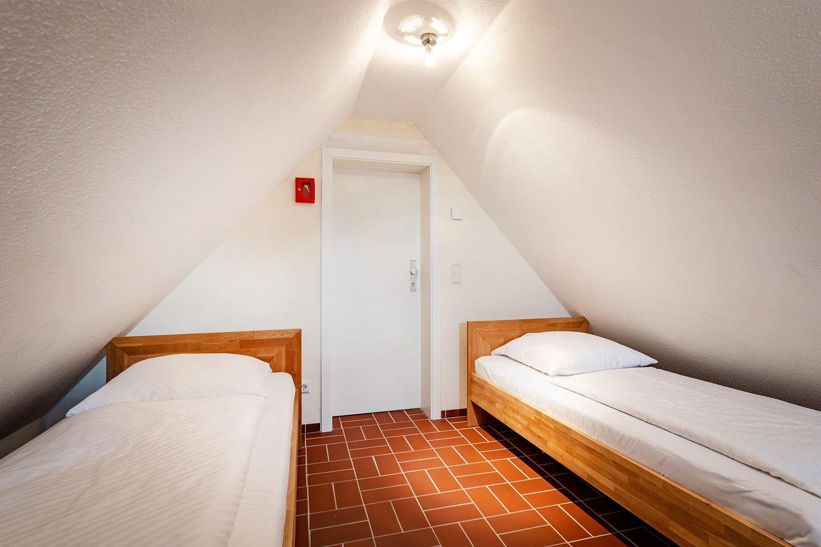 Zwei Einzelbetten in einem Dachzimmer mit Holzrahmen und Terrakottaboden.