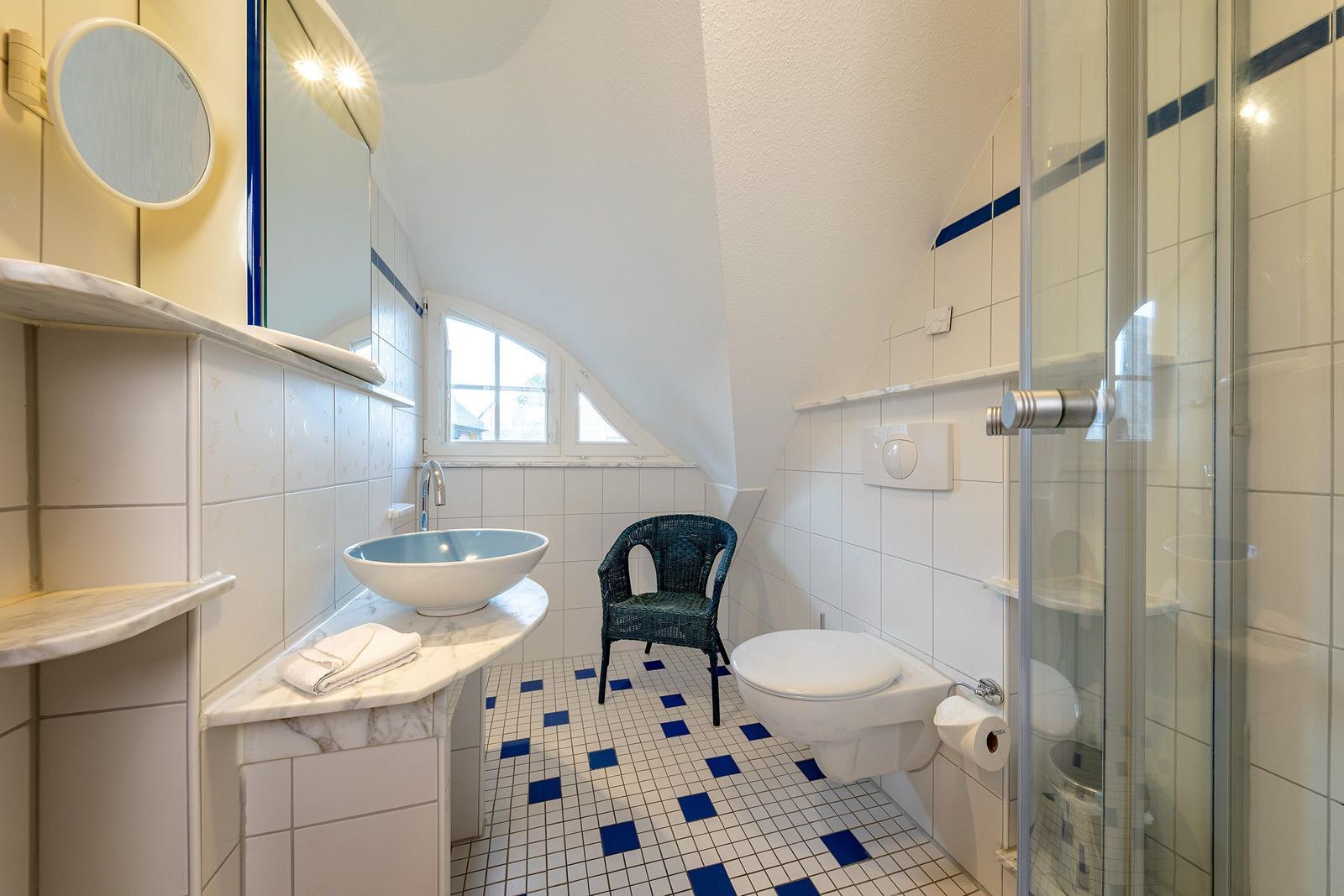 Badezimmer mit Dusche, WC, Waschbecken und Stuhl unter Dachschrägen.