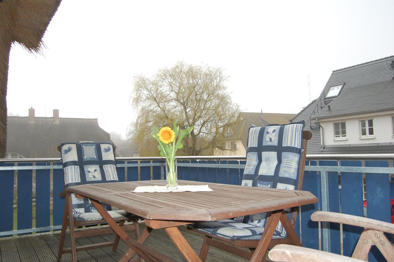 Terrasse mit Holztisch, zwei Stühlen und einer Blume im Glas.