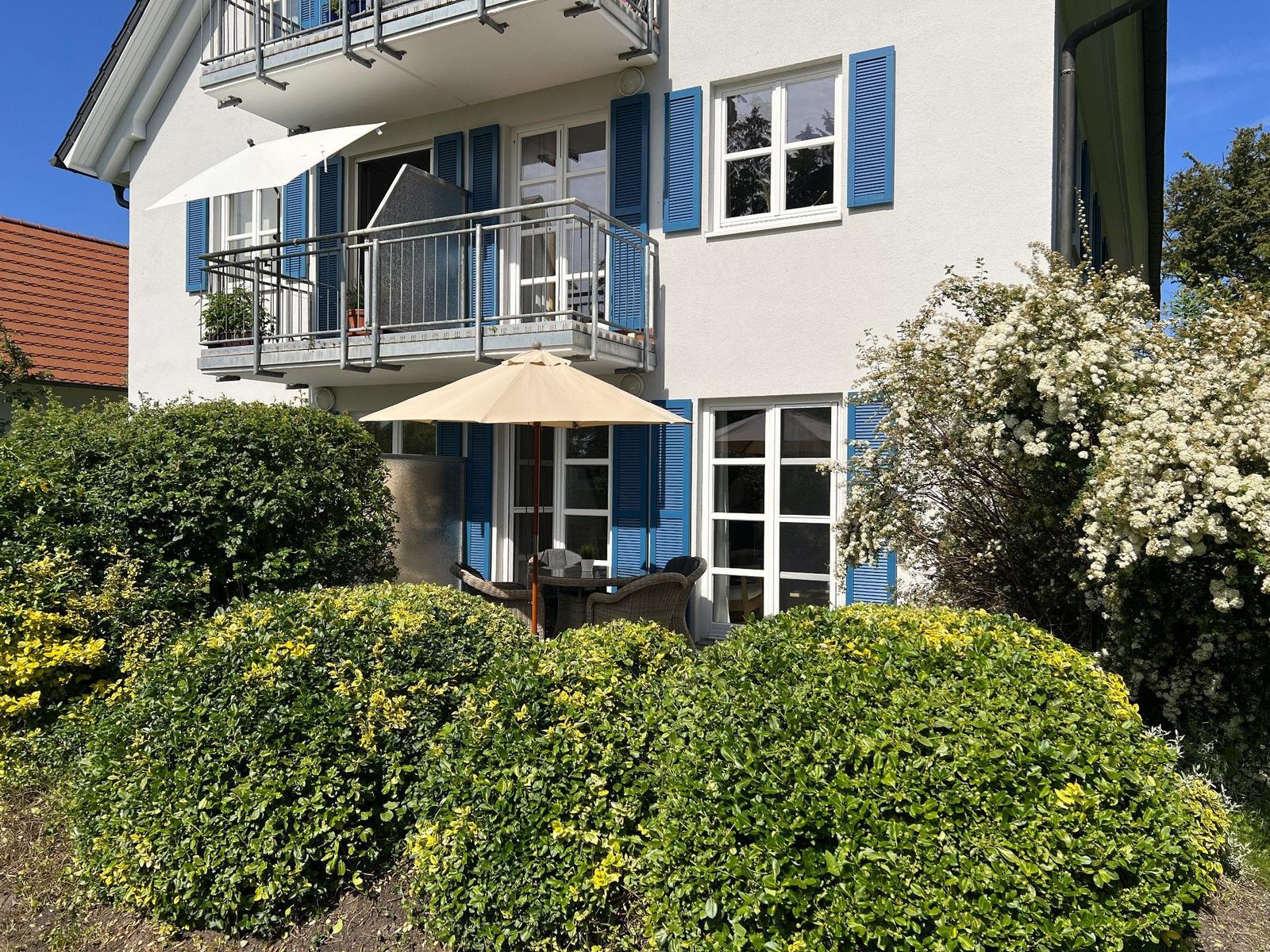 Wohnhaus mit Balkon und Gartenbereich mit Sonnenschirm und Sitzgelegenheit.