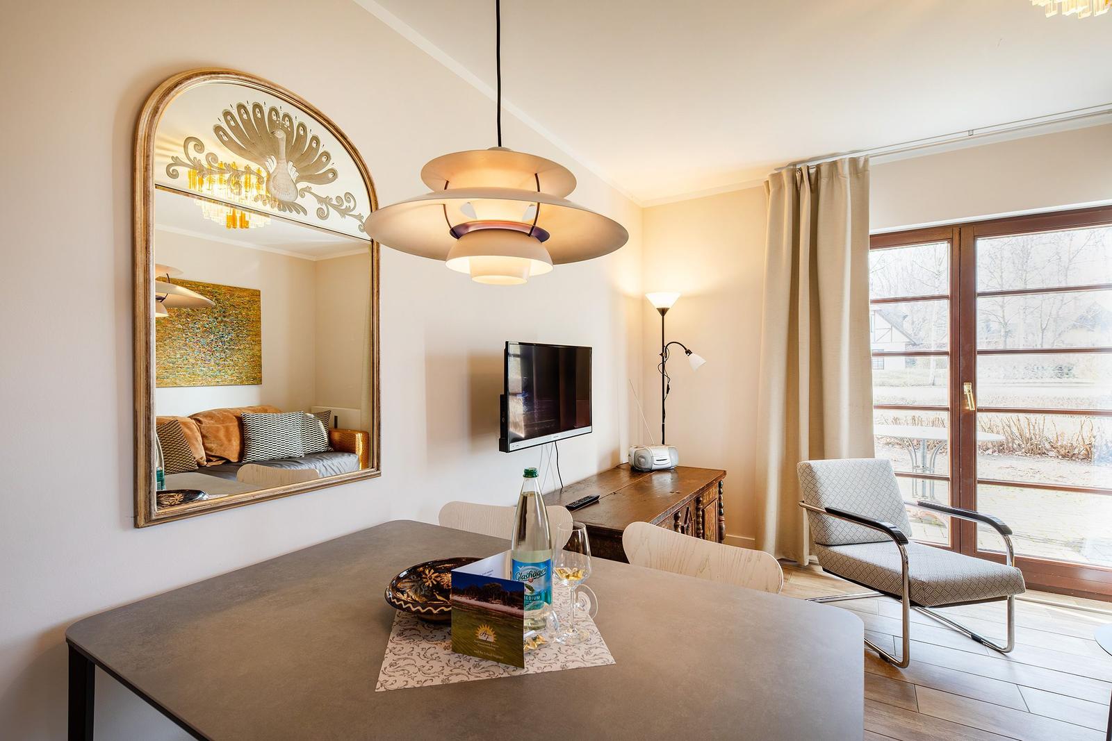 Essbereich mit Tisch, Stühlen und Fernseher. Spiegel und Fenster sichtbar.