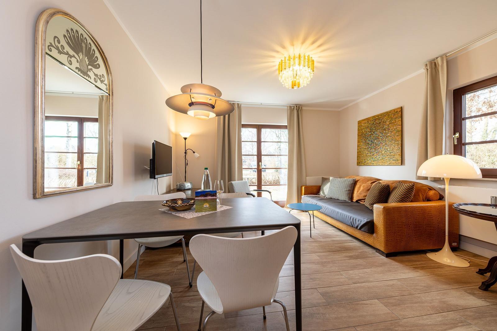 Wohn- und Essbereich mit Sofa, Tisch und Stühlen sowie Fenstern und Deckenleuchten.