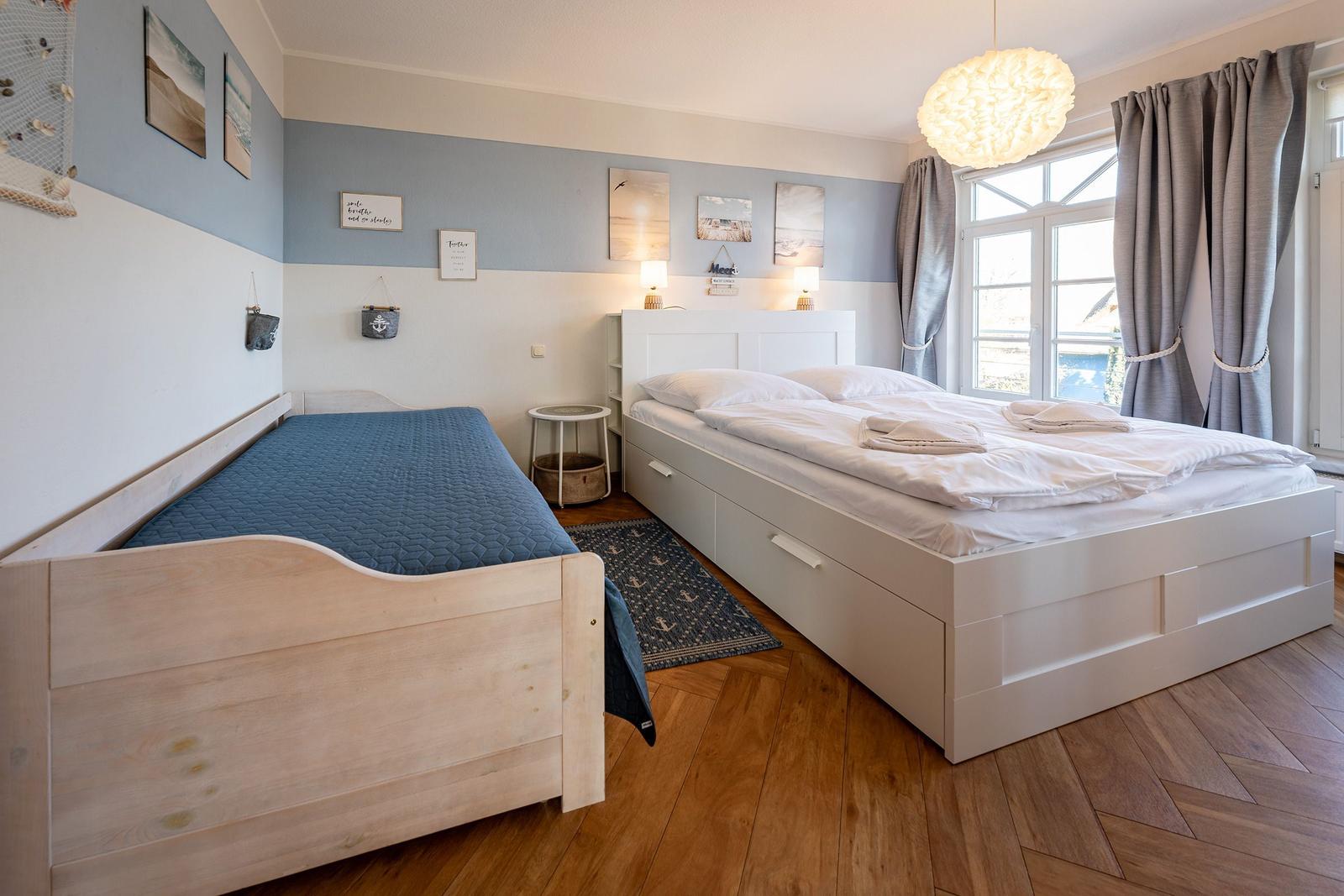 Zimmer mit zwei Betten, Holzboden und Fenster mit Vorhängen.