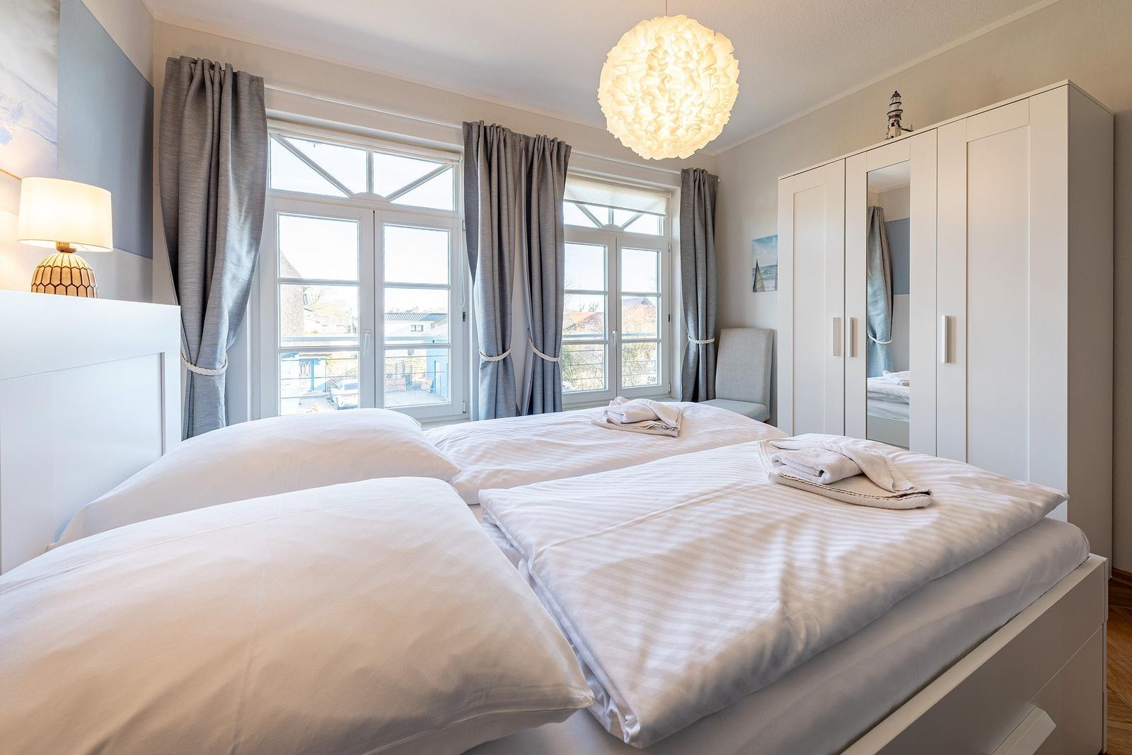 Schlafzimmer mit Doppelbett, Fenstern und Kleiderschrank.