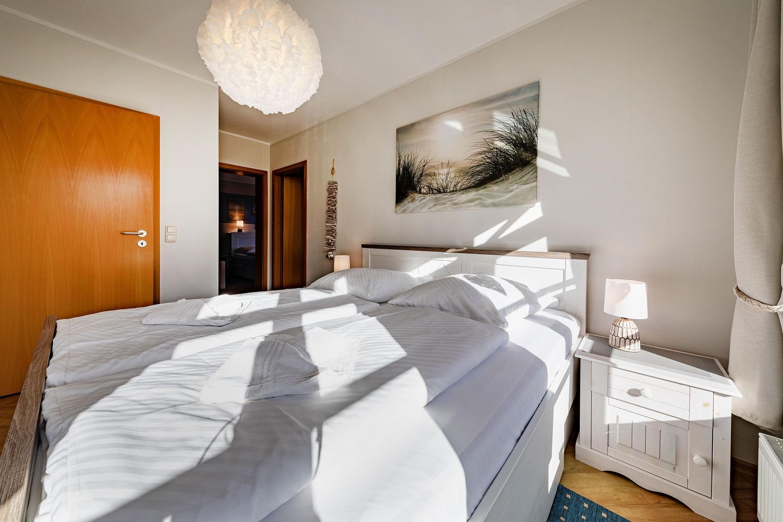 Schlafzimmer mit Doppelbett, Nachttisch und Wandbild. Deckenleuchte und Holztür sichtbar.