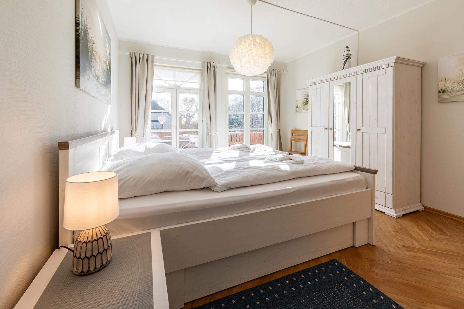 Schlafzimmer mit Doppelbett, Kleiderschrank und Fenster zum Balkon.