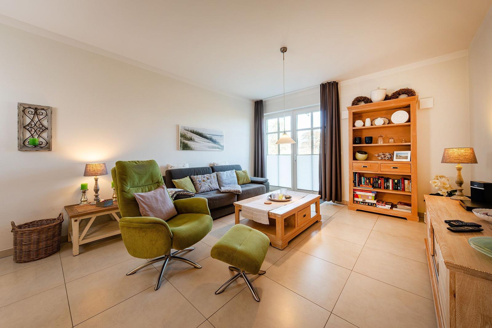 Wohnzimmer mit grünem Sessel, Sofa, Holzmöbeln und Fenster zur Aussicht.