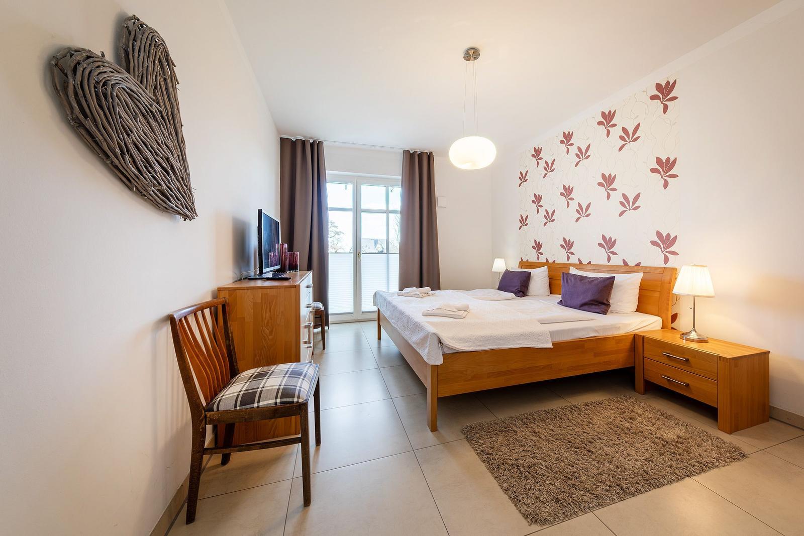 Schlafzimmer mit Doppelbett, Schreibtisch, Fernseher und Balkonansicht.