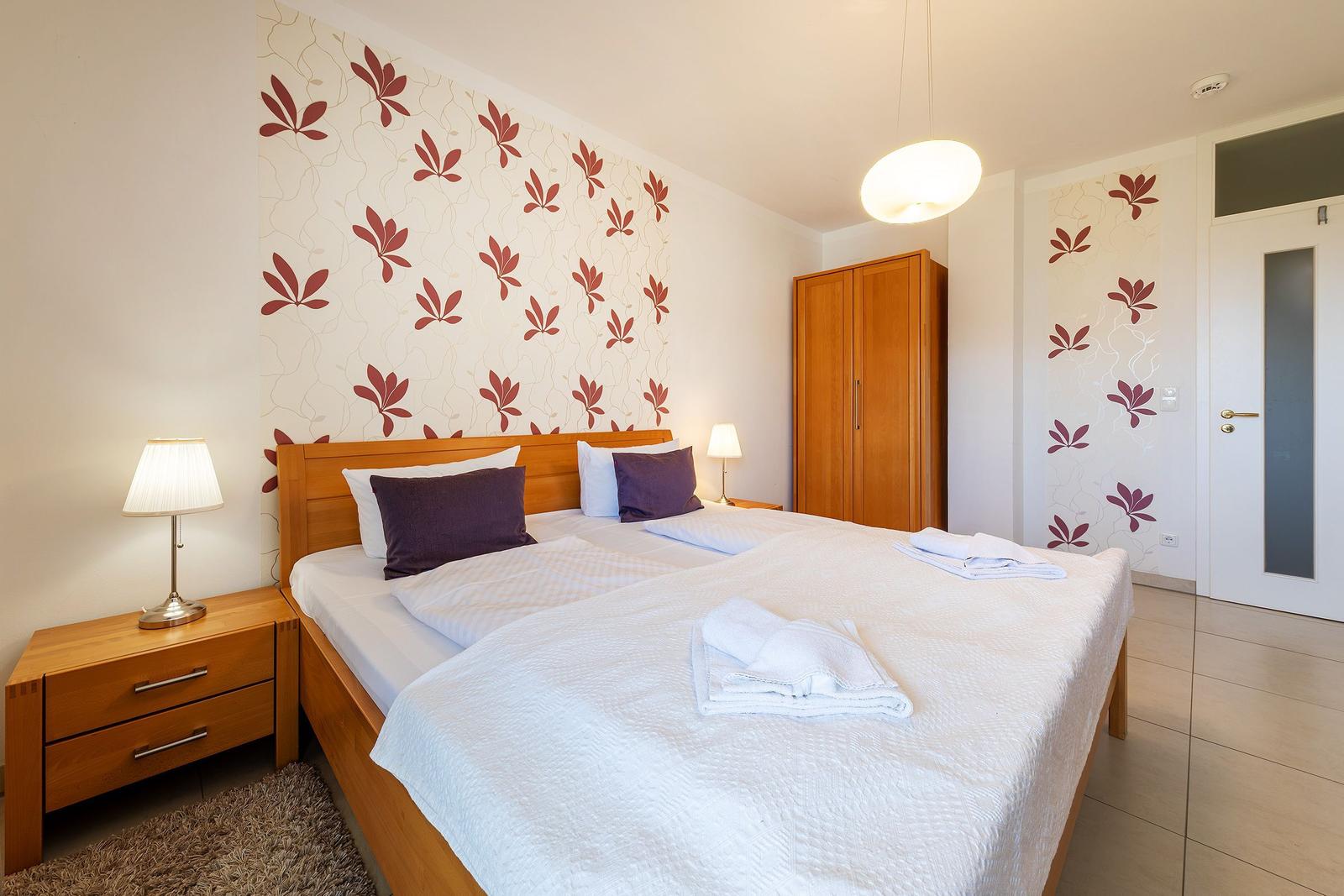 Schlafzimmer mit Doppelbett, Holzmöbel und floraler Wandtapete.