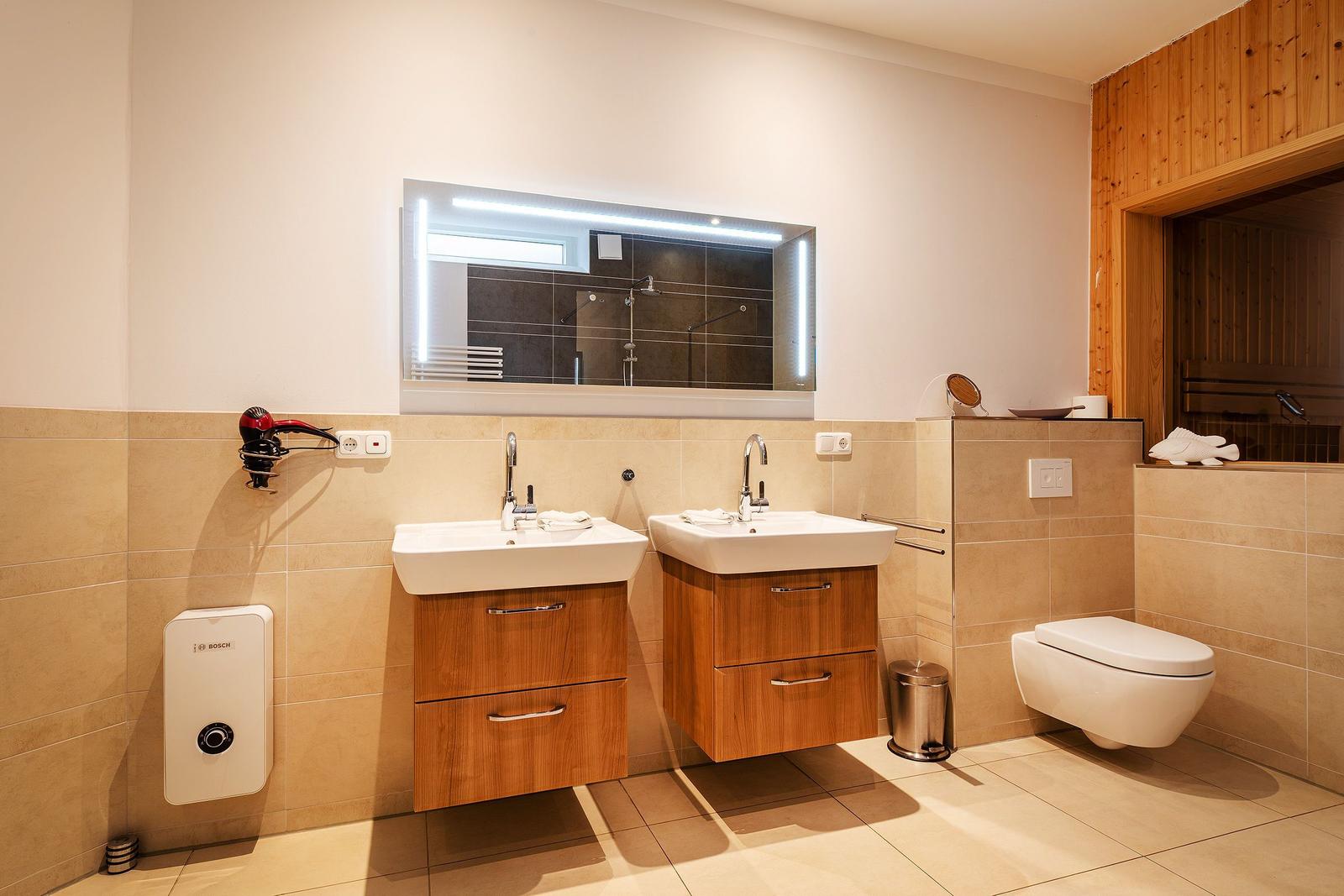 Bad mit zwei Waschbecken, Spiegel und Toilette. Holzwand und Dusche sichtbar.
