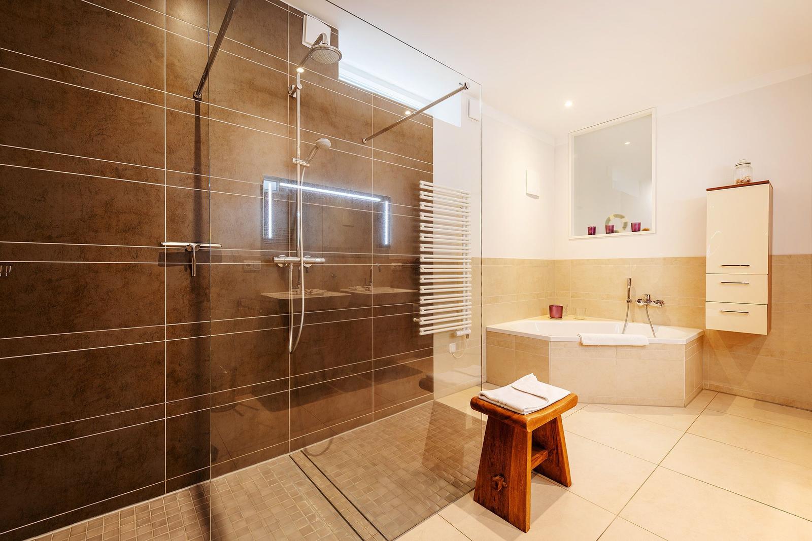 Dusche mit Glaswand, Badewanne und Holzstuhl
