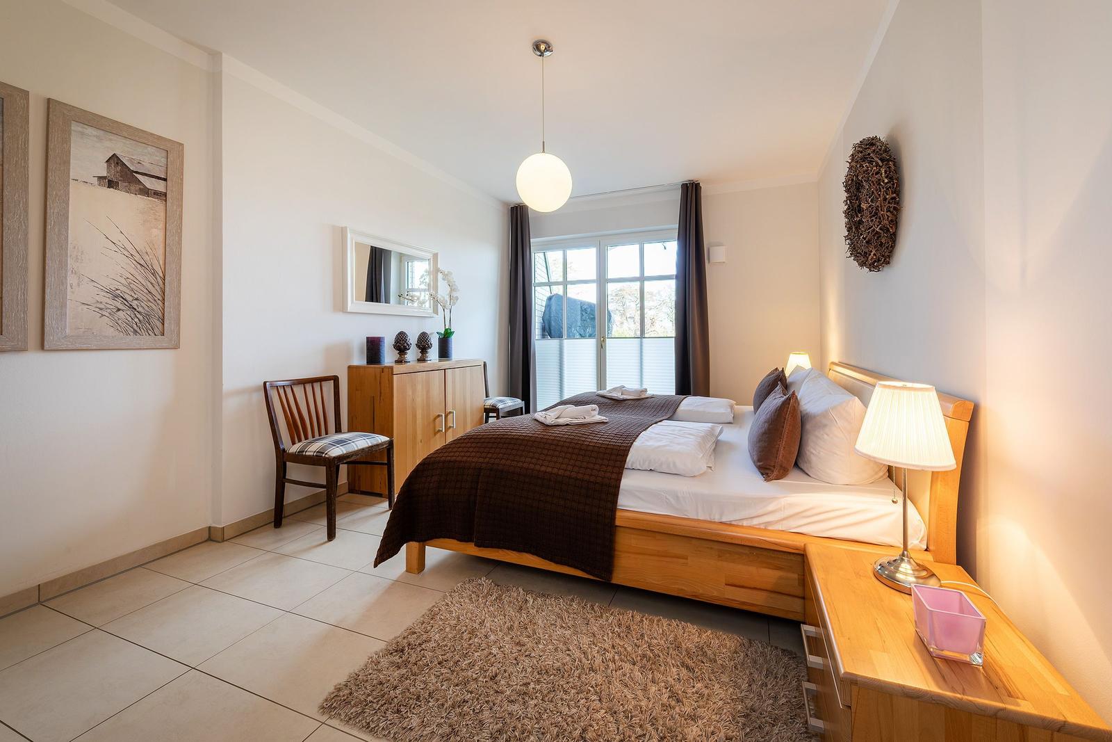 Schlafzimmer mit Holzbett, Nachttisch, Stuhl und Fenster mit Blick.