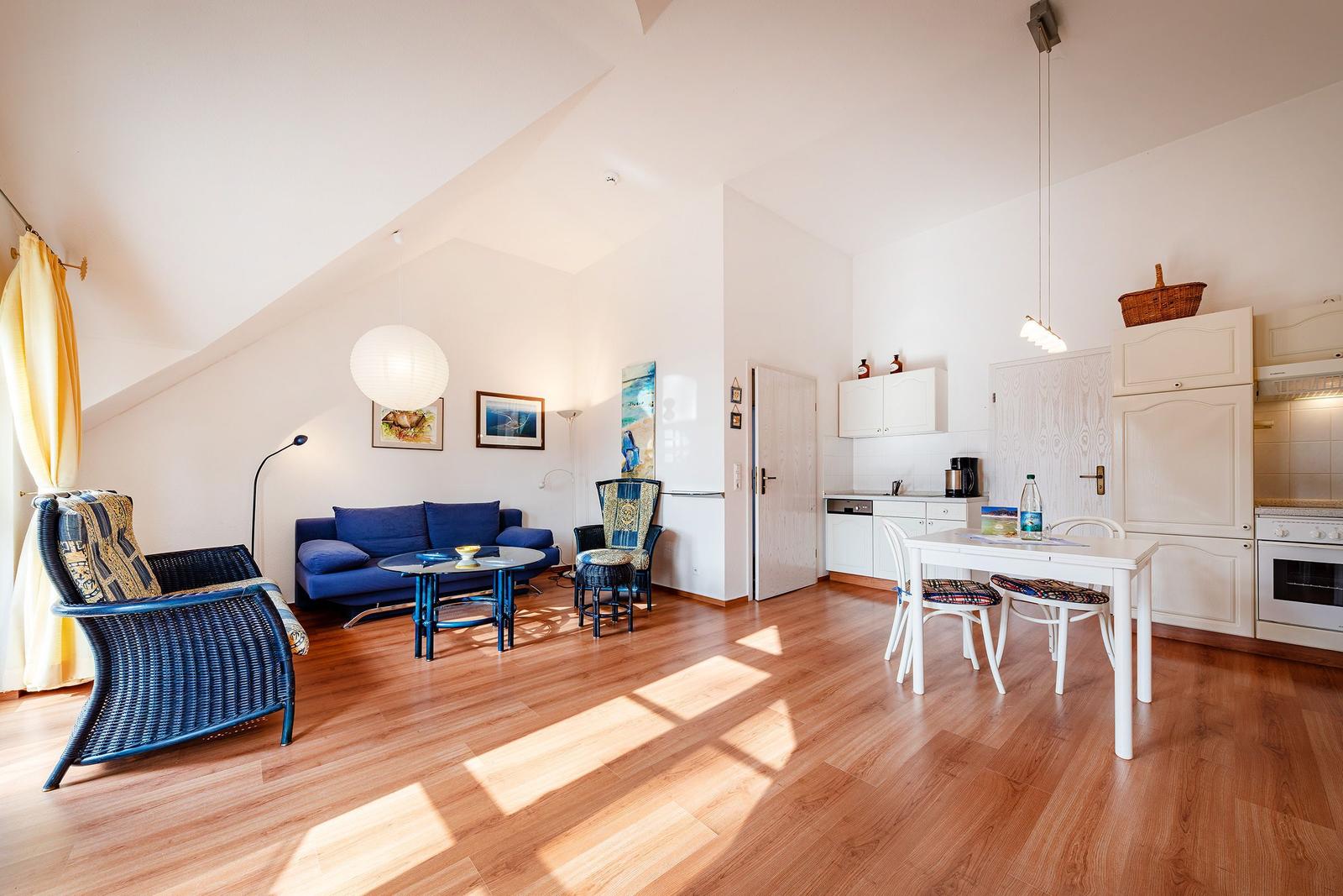 Wohnküche mit Holzboden, blauem Sofa, Esstisch und Küchenschränken.